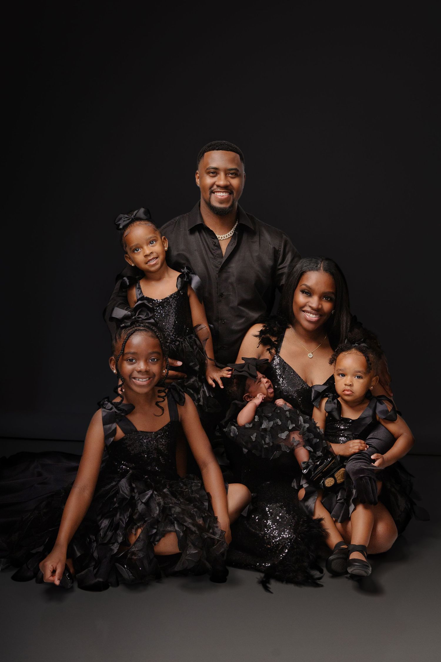 Studio portrait of group wearing matching black formal attire against dark background.