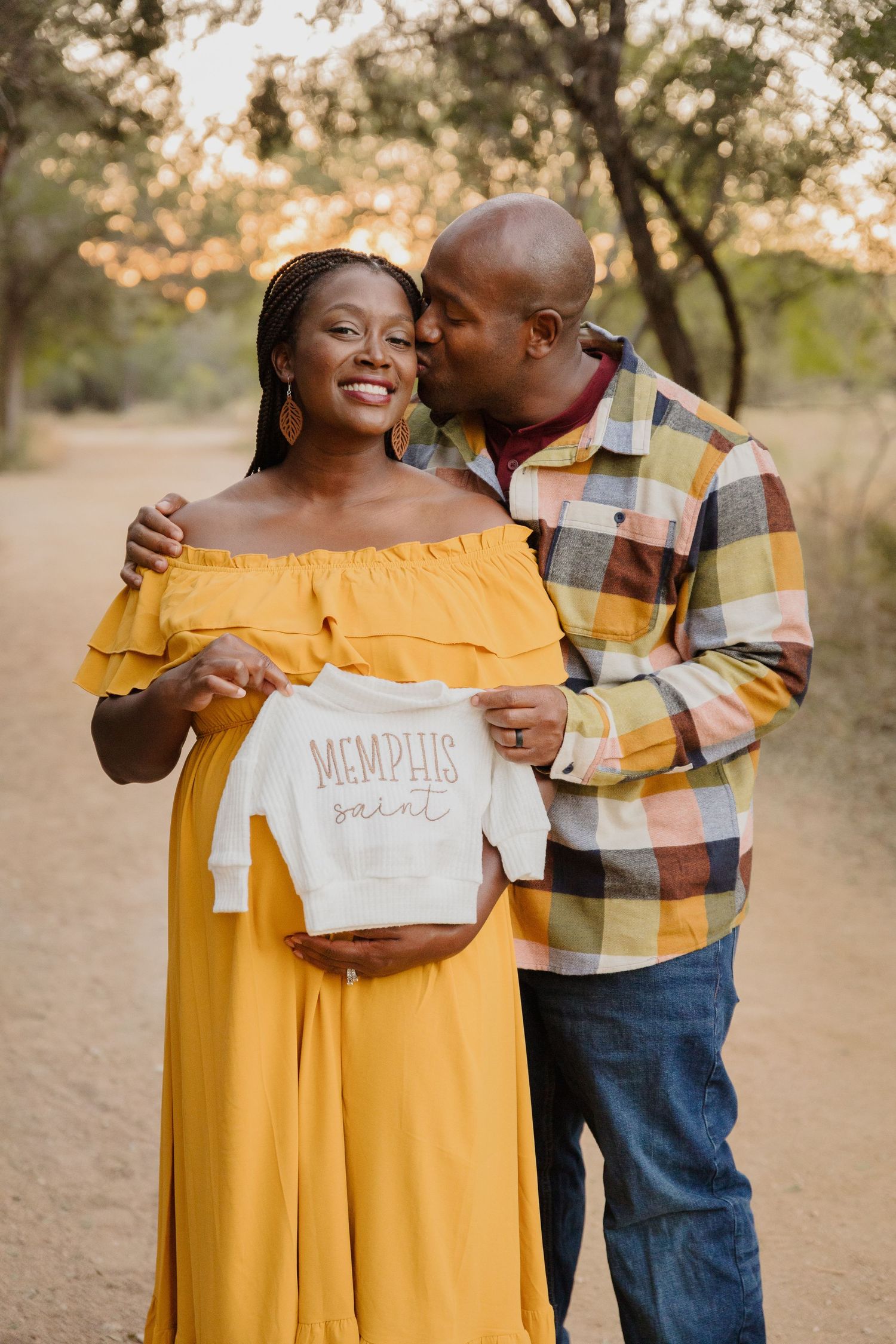 Couple holds baby onesie during outdoor maternity photoshoot.