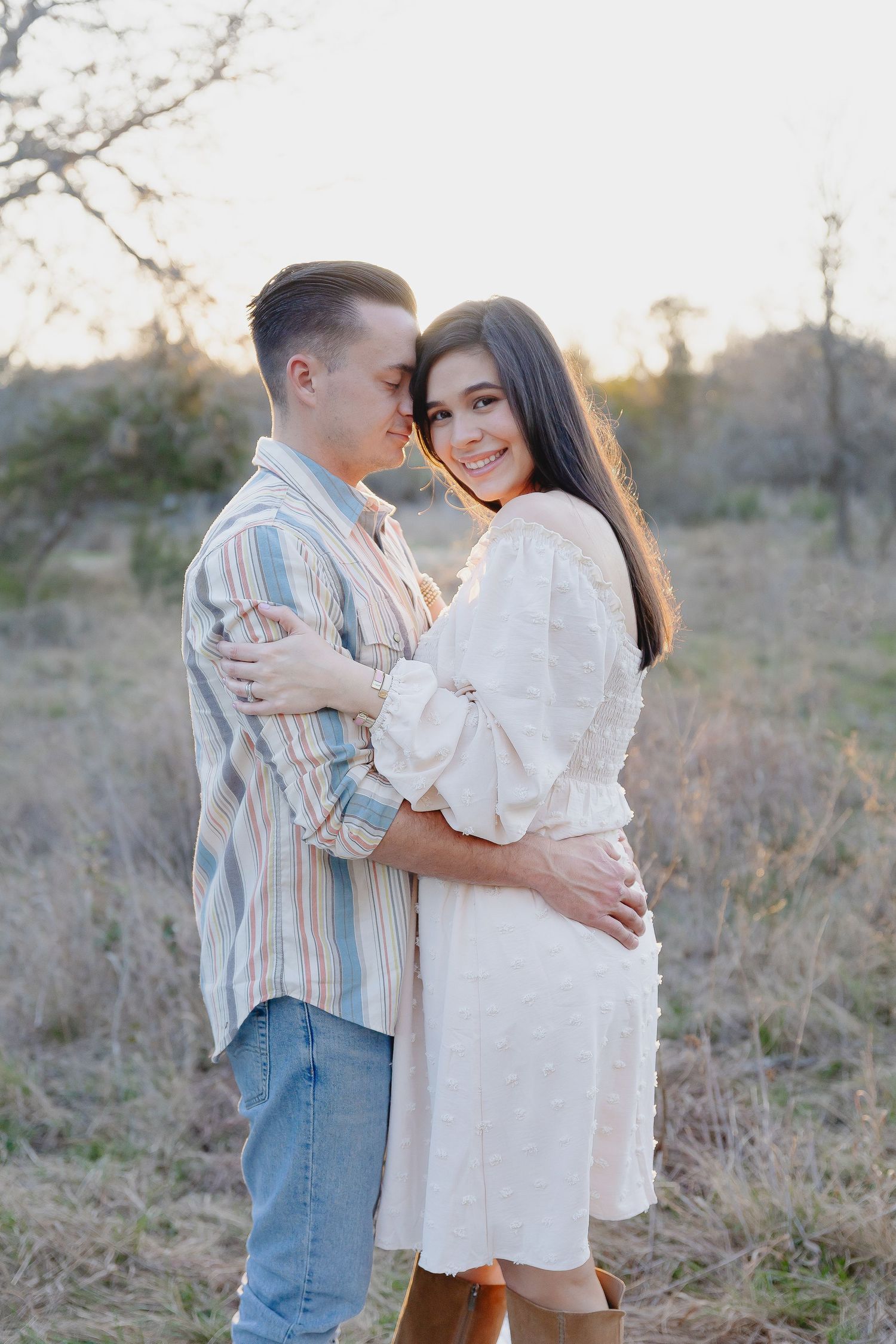 A romantic outdoor portrait of a couple embracing in casual attire during golden hour.