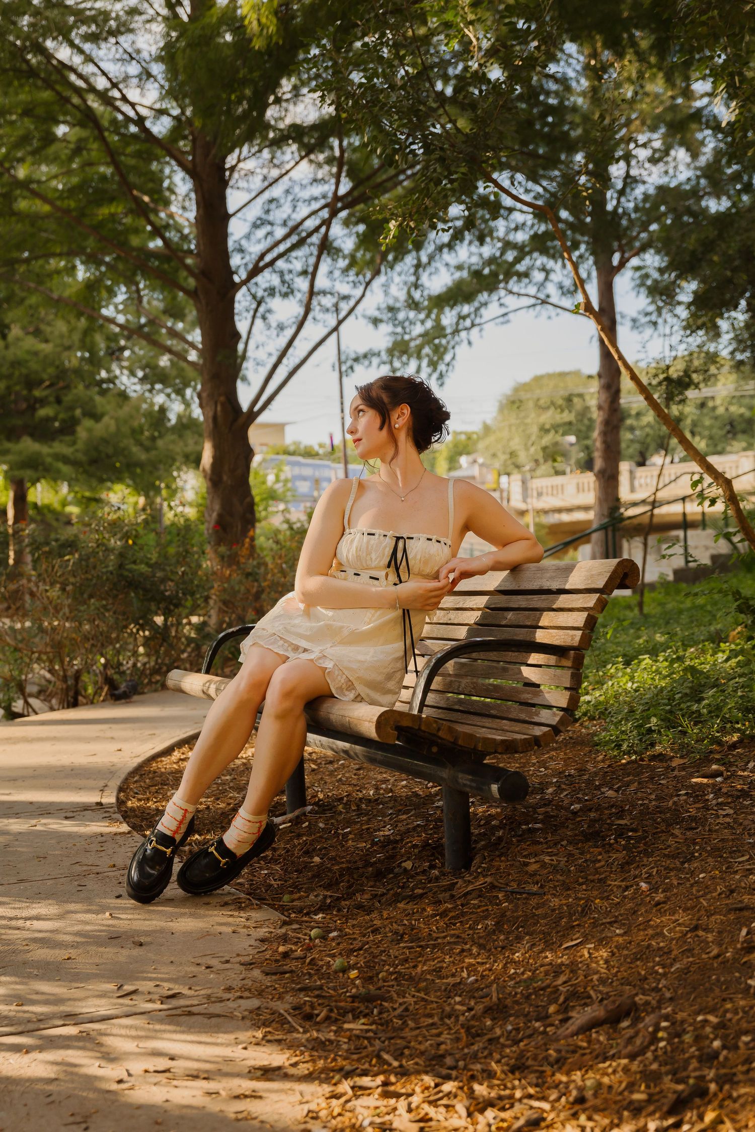 Woman relaxing on park bench in sundress during golden hour.