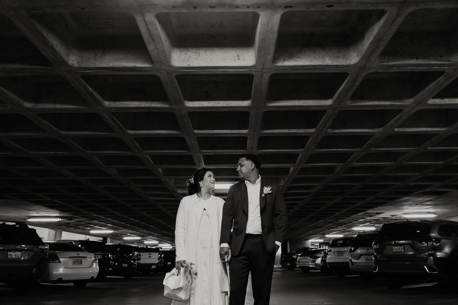 Couple stands together in dramatically lit parking garage.
