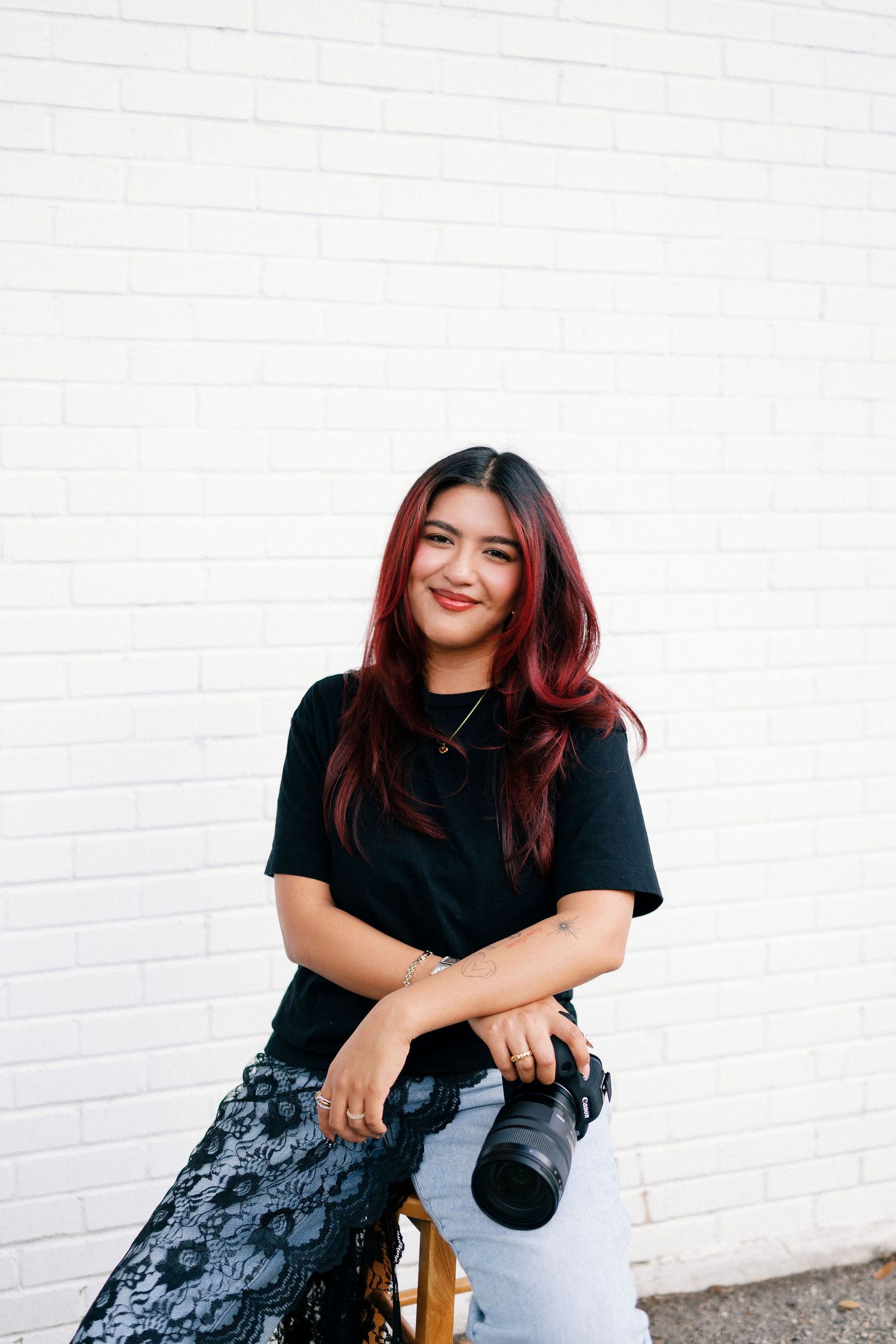 Photographer holding camera poses casually against white brick wall in three similar shots.