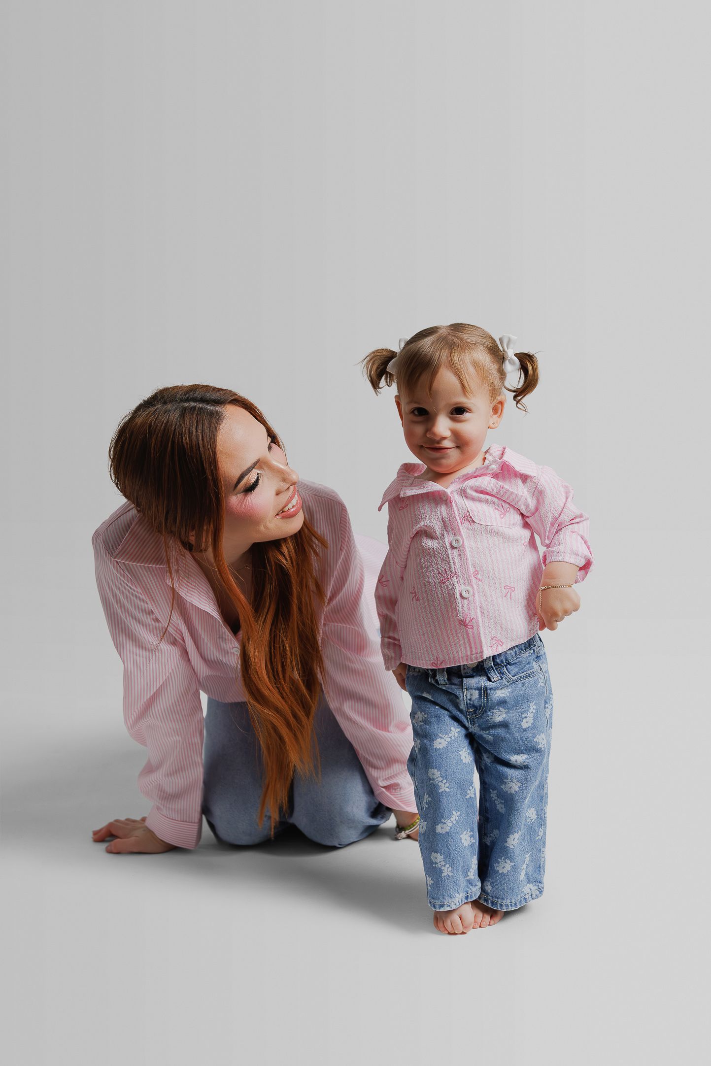 Parent and toddler in matching pink and denim outfits share playful moments in a studio photo sequence.
