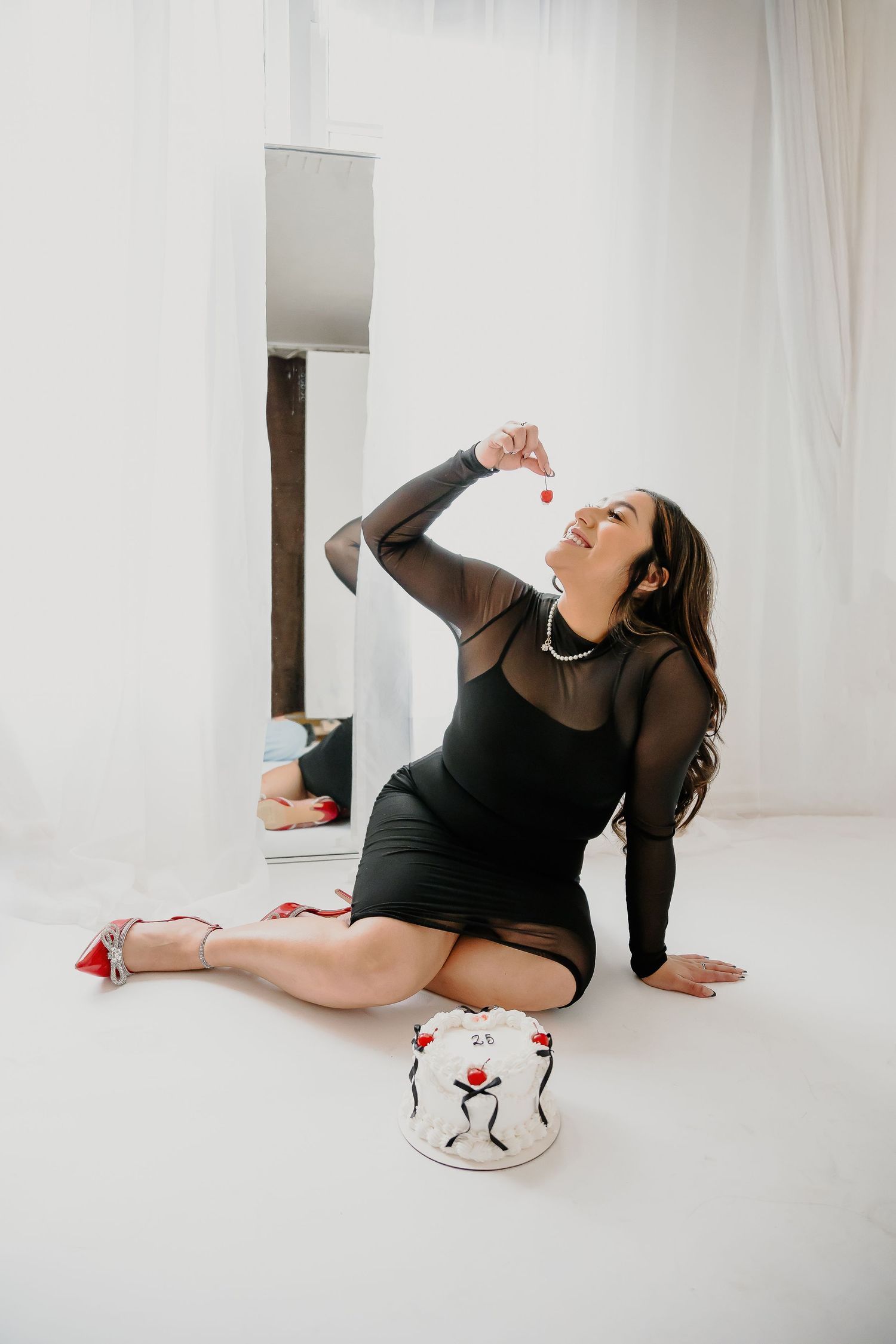 A stylish portrait featuring a black mesh dress and decorative cake in minimalist white setting.