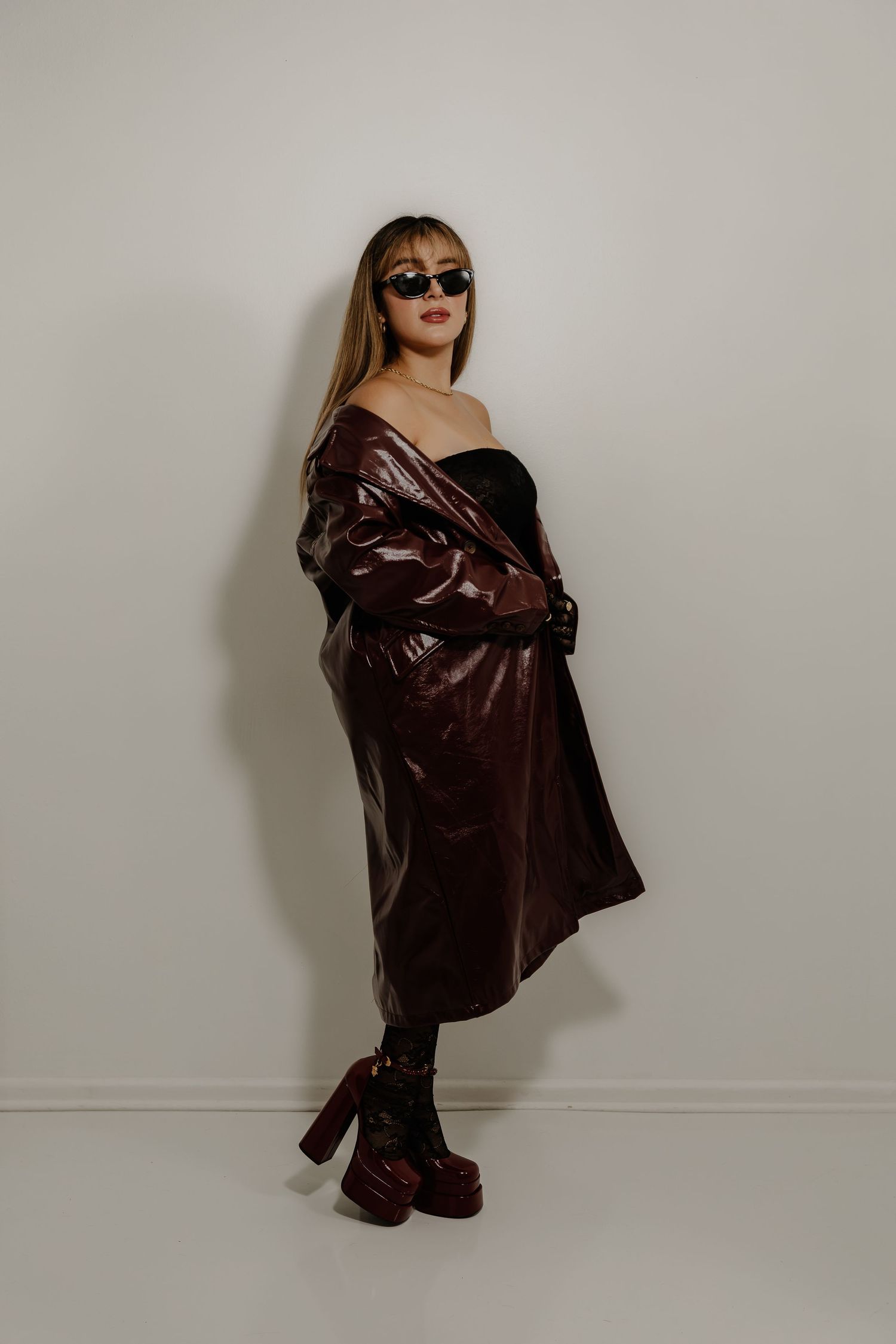 Fashionable pose in burgundy leather trench coat, sunglasses and platform boots.