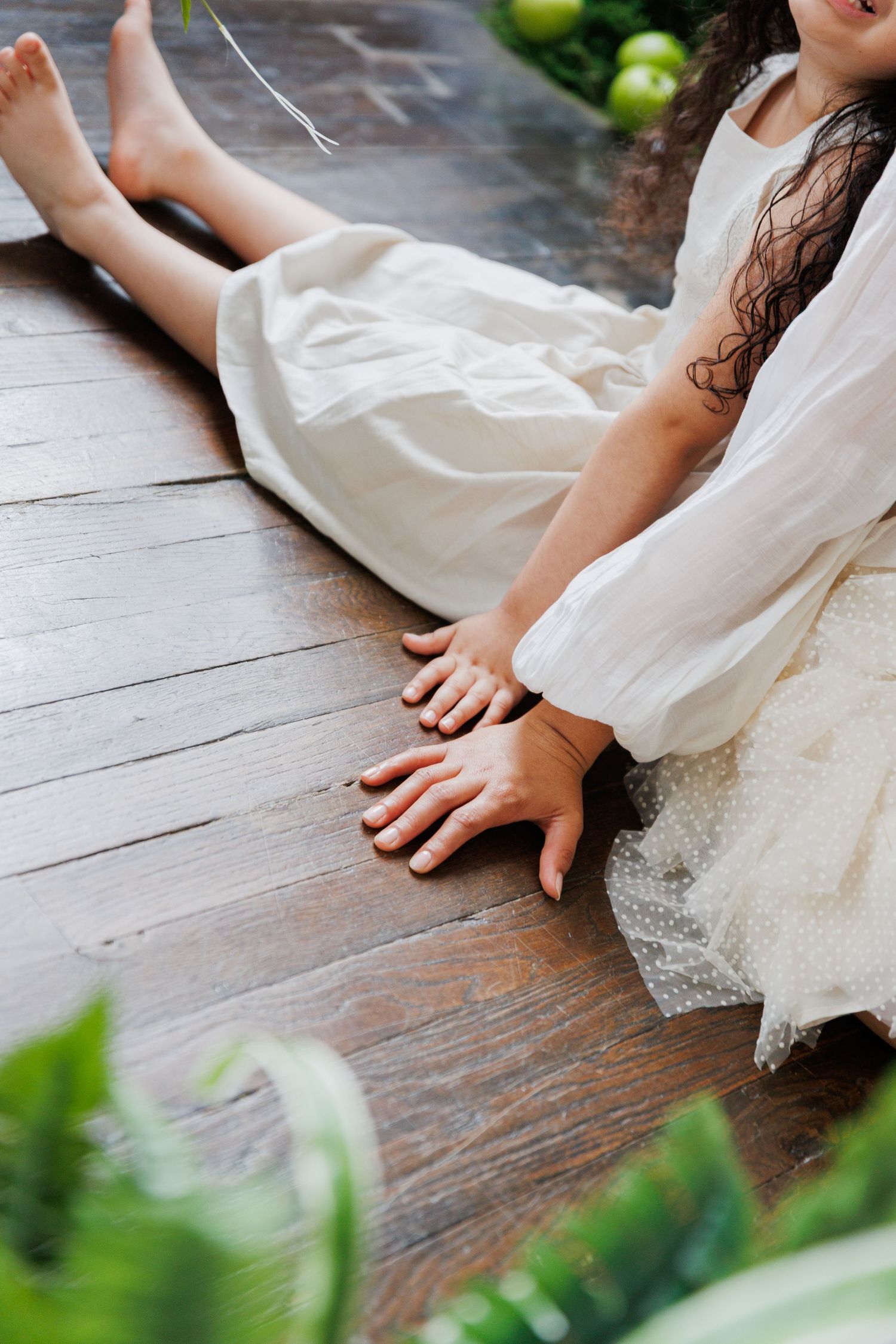 Close-up detail shots of hands and fabric against dark wooden flooring with green foliage in soft natural lighting.