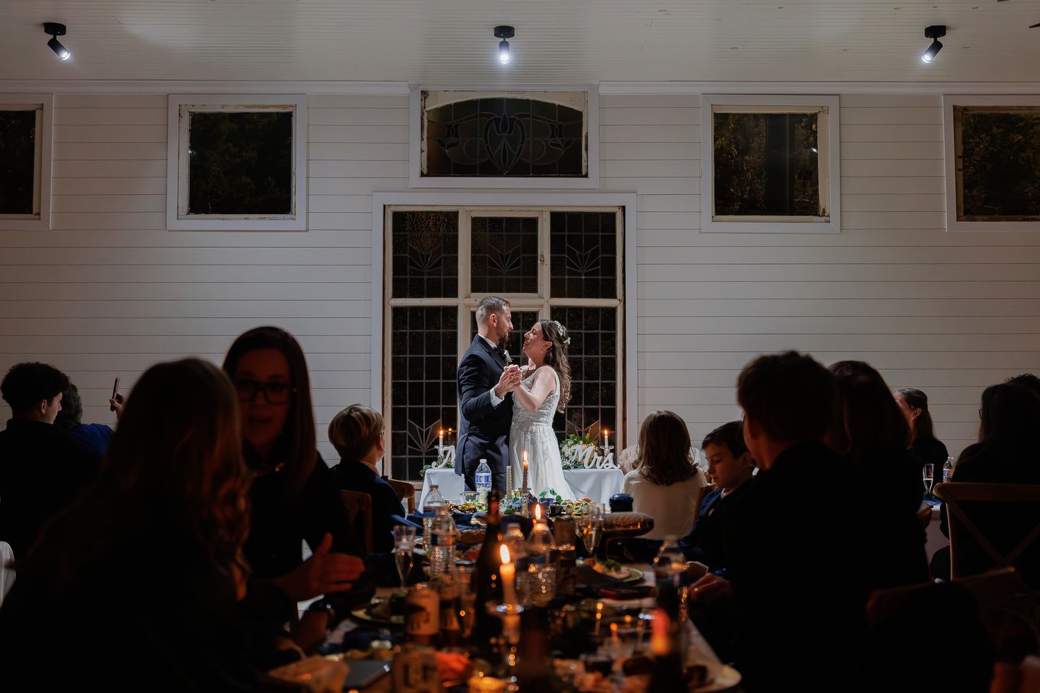 A dimly lit wedding reception venue with guests seated at tables illuminated by warm candlelight.