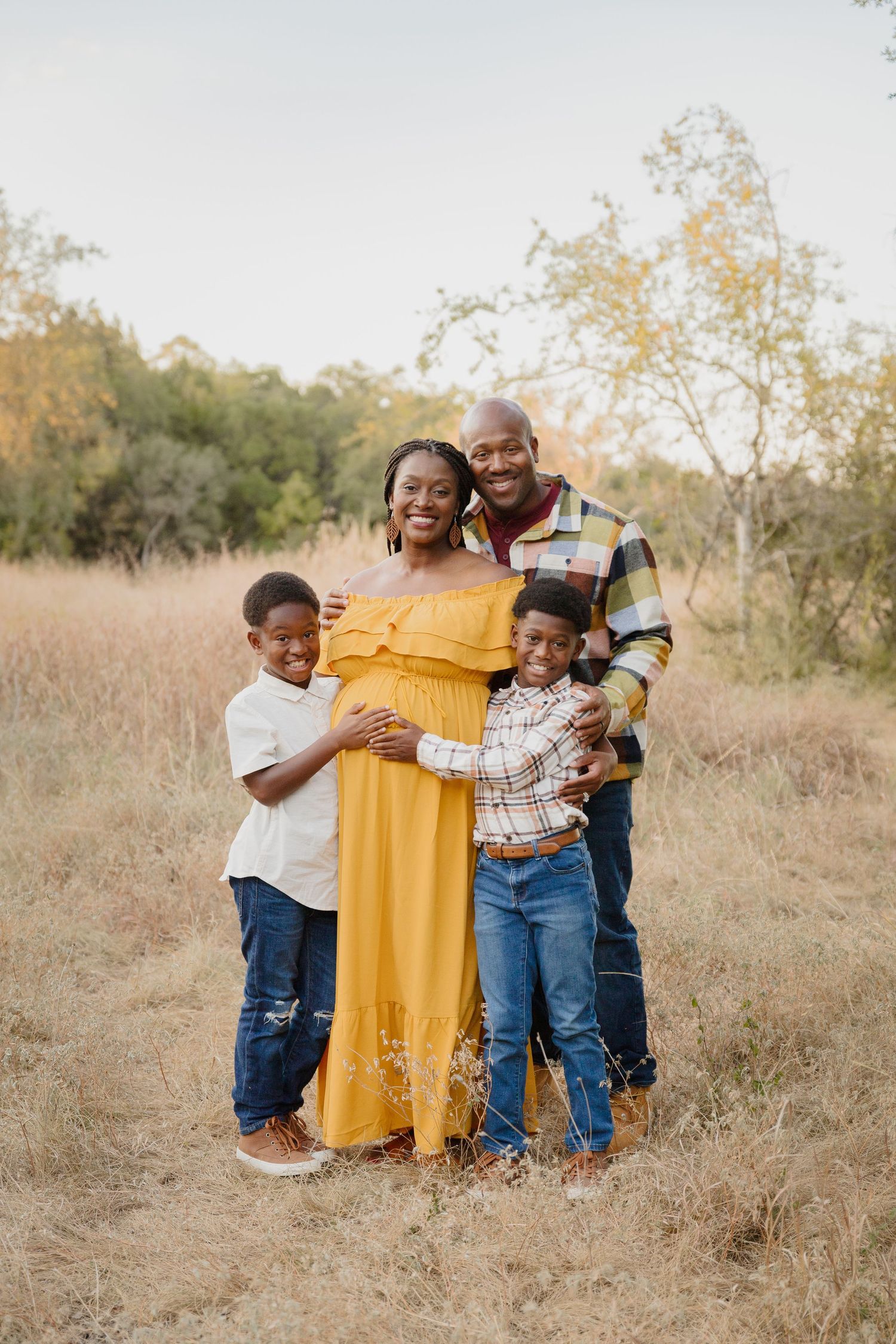 A happy family of four poses together in a golden field during autumn.