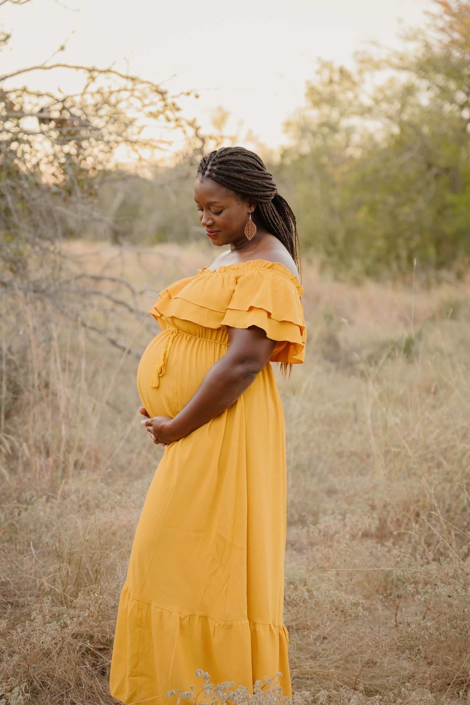 Woman in yellow maxi dress showcasing baby bump in outdoor nature setting.