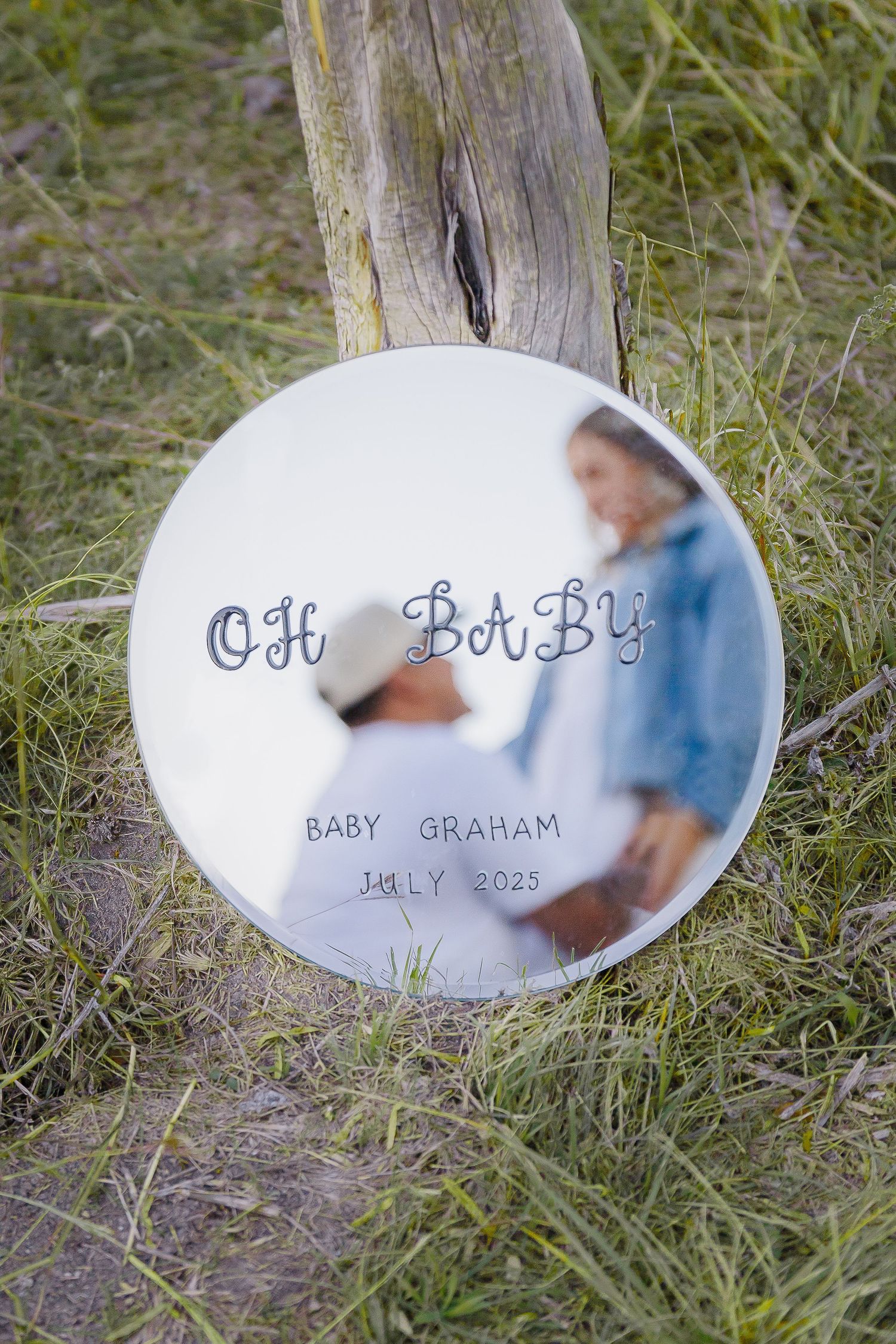 Decorative pregnancy announcement disc with 'Oh Baby' text placed against weathered wood.