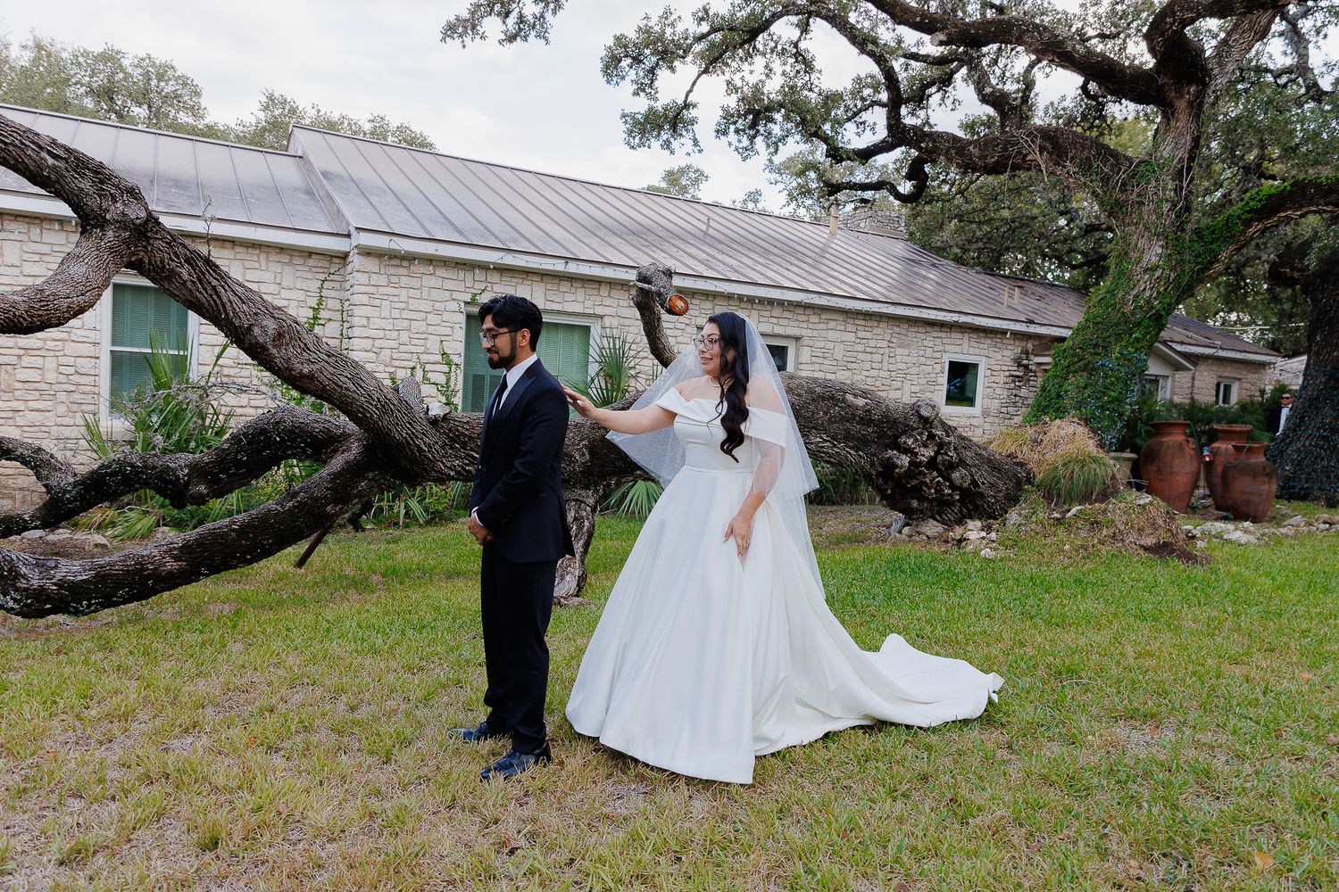 A wedding couple poses for romantic photos under sprawling oak trees on a rustic property.