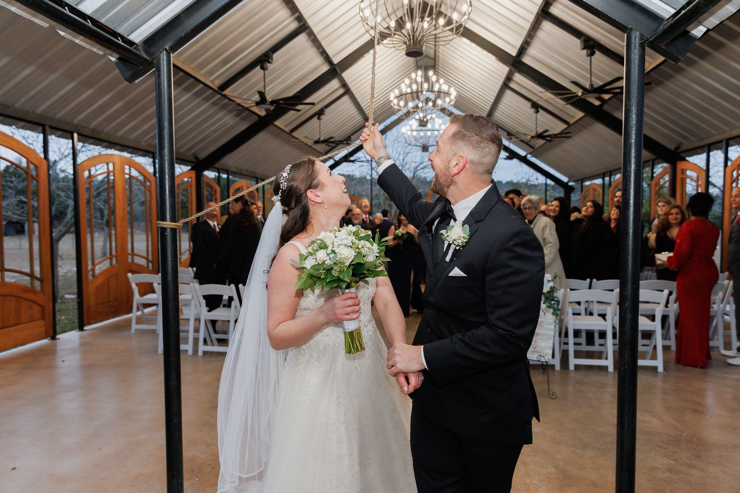 Couple shares a romantic dance moment under an elegant chandelier in a rustic venue with exposed beams.