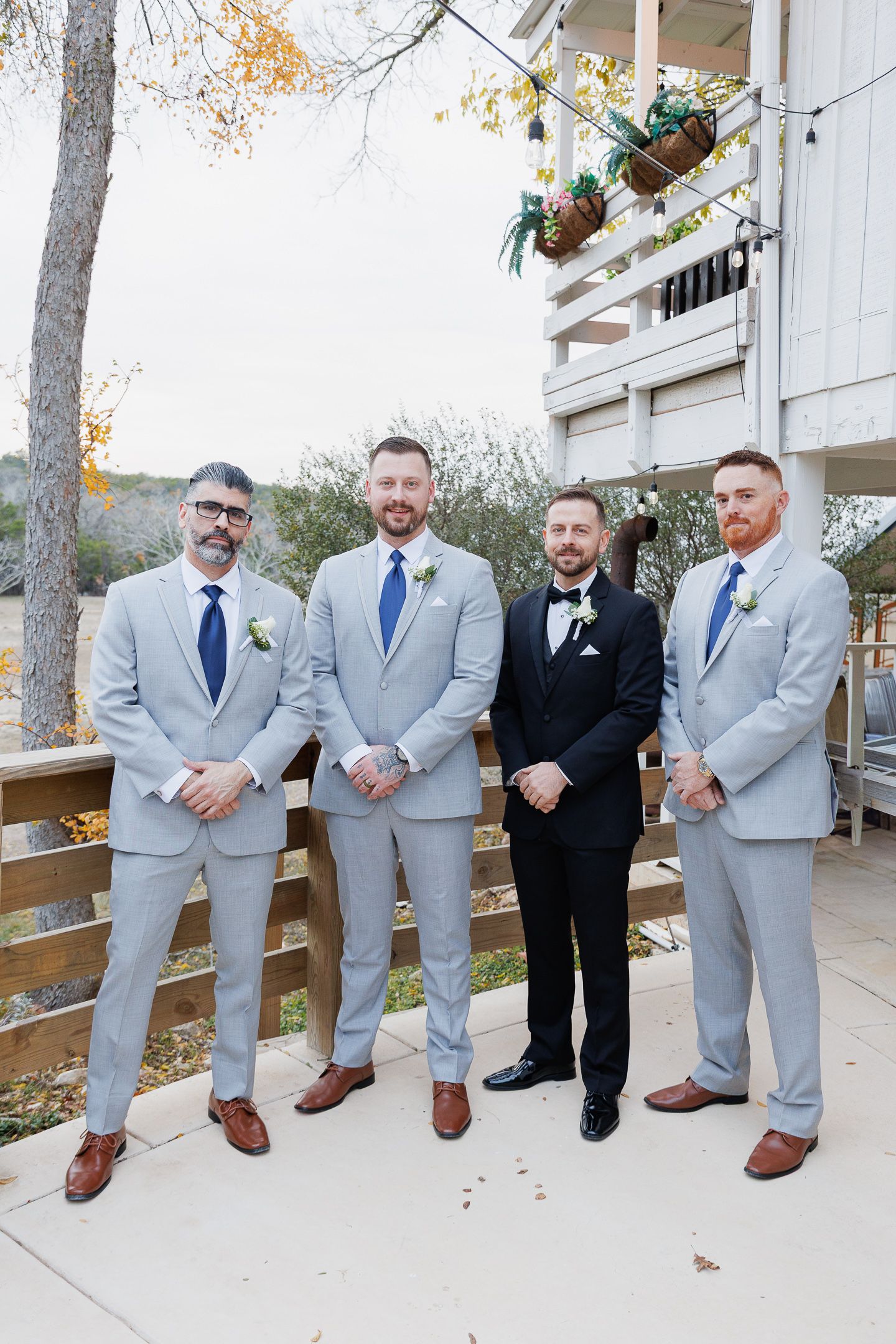 Groomsmen in light gray suits and one in black pose casually on outdoor stairs at a wedding venue.