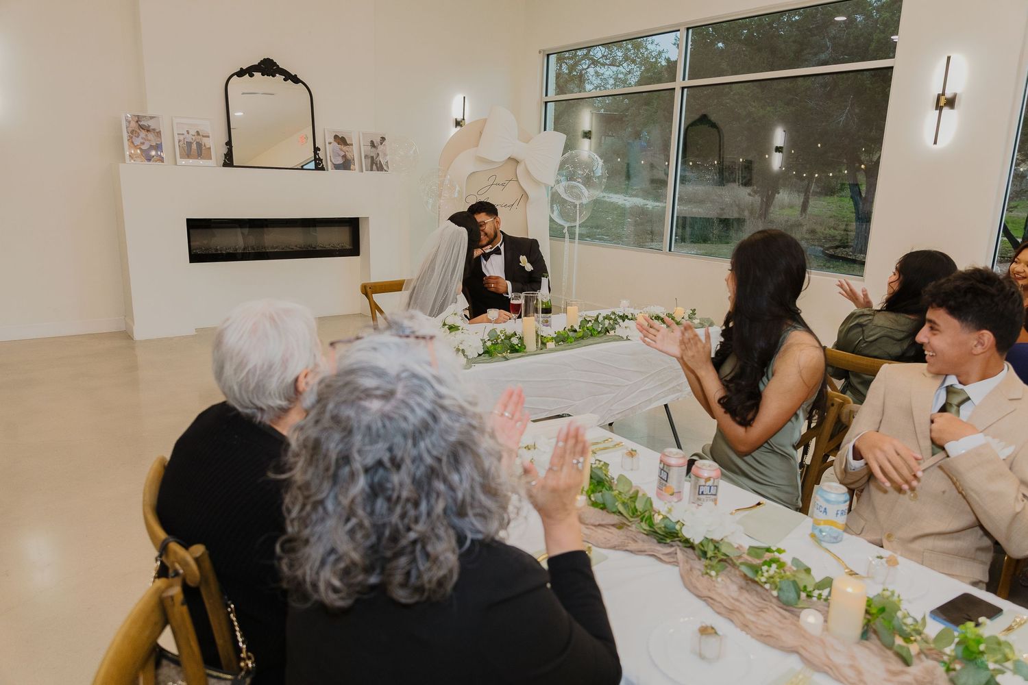Wedding reception table with guests enjoying dinner in a modern venue with white decor.