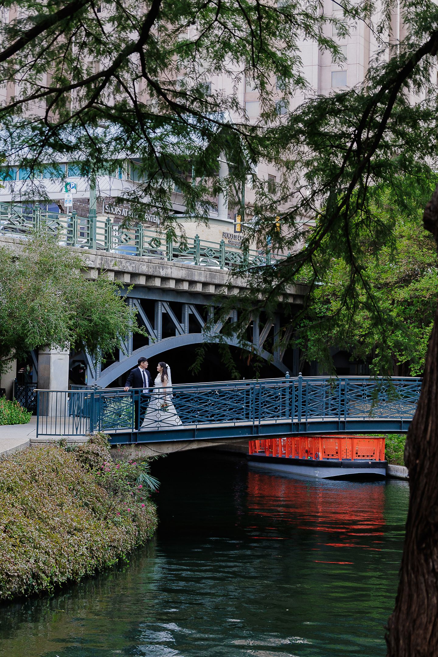 Historic bridge spans over the San Antonio River with lush green trees framing the waterway.
