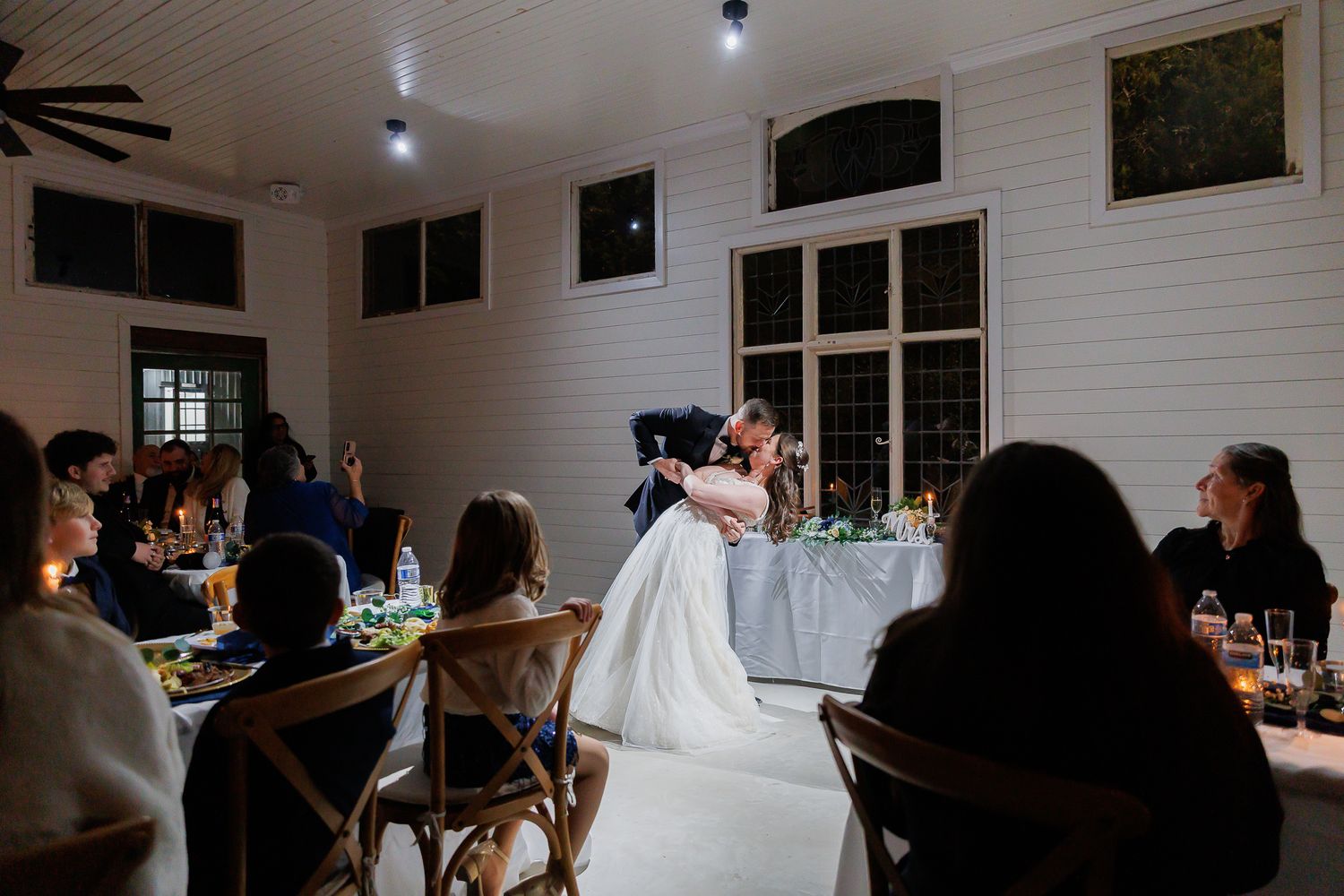 Wedding reception in a bright white barn-style venue with guests seated at tables.