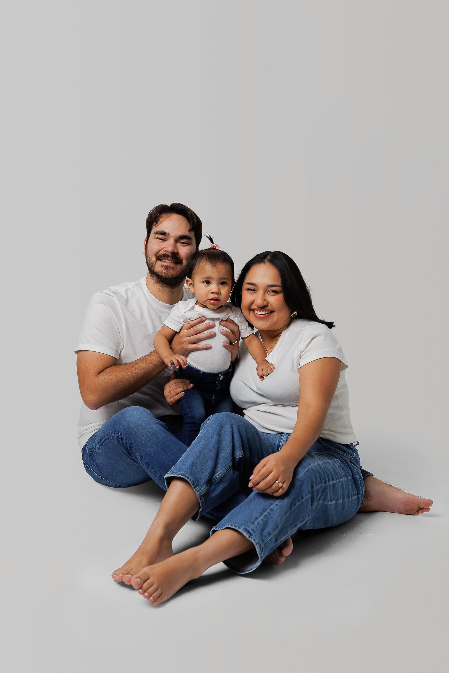 A family in matching white shirts and jeans sits together on a white background in four similar poses.