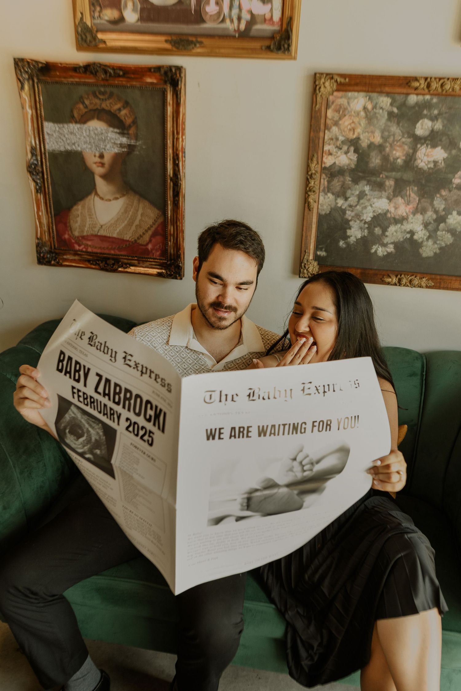 Couple reading customized newspaper pregnancy announcement on green couch.