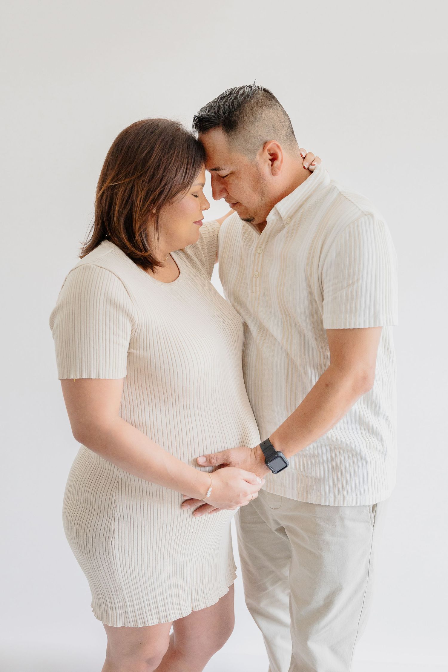 Couple in matching cream outfits share an intimate moment against white background.