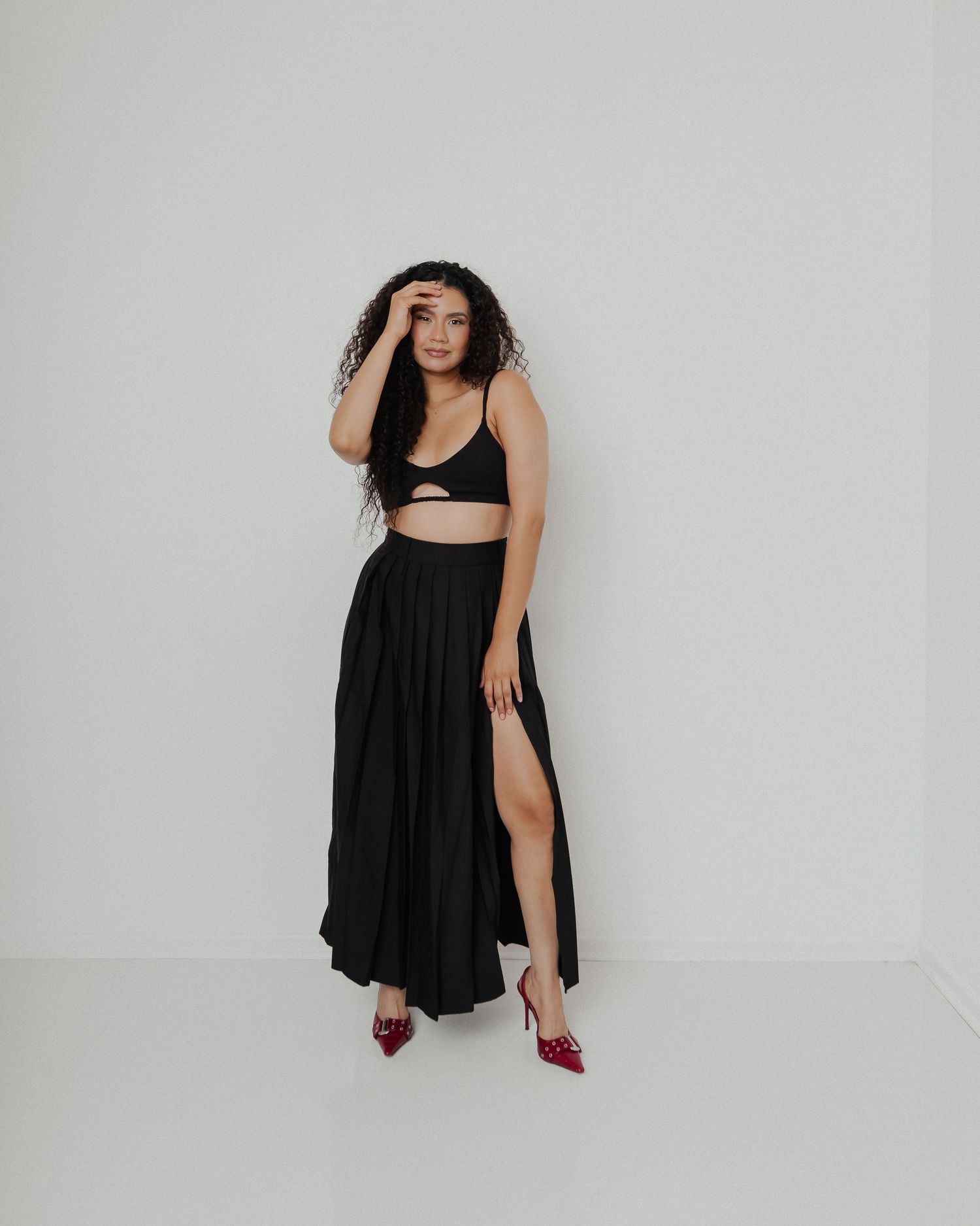 A model poses in a black two-piece ensemble with red heels against a minimalist white backdrop.