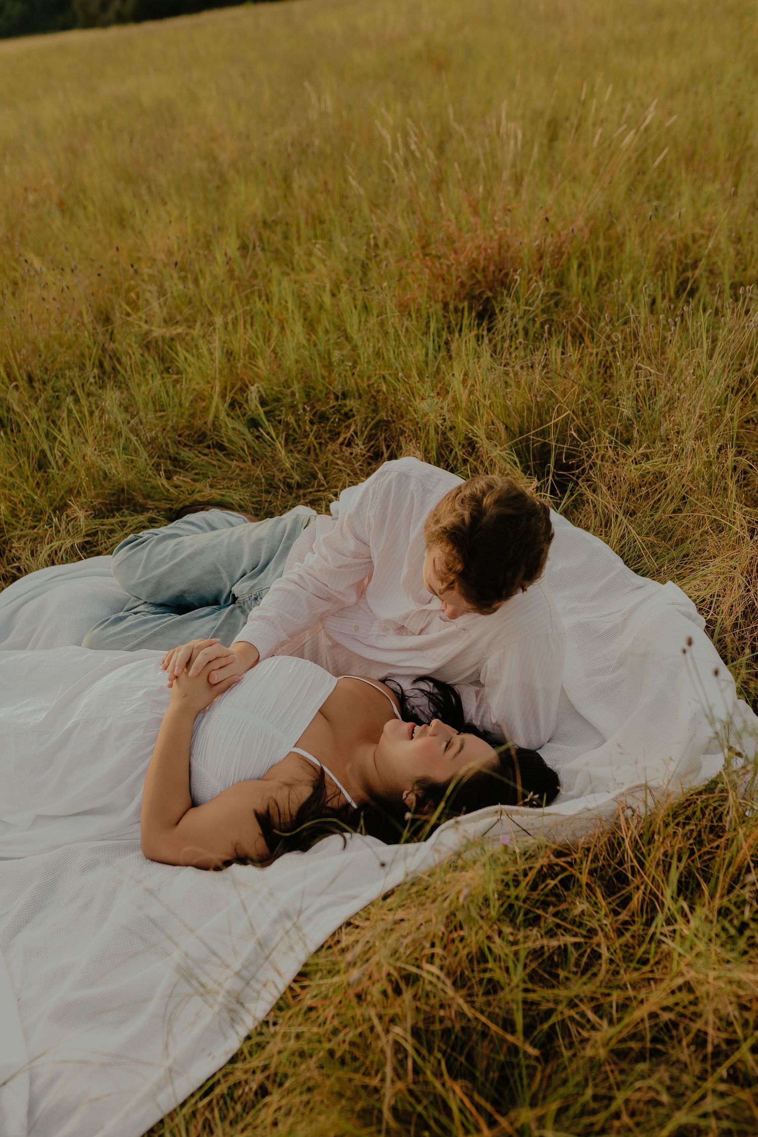 Couple lying together on a white blanket in tall golden grass.