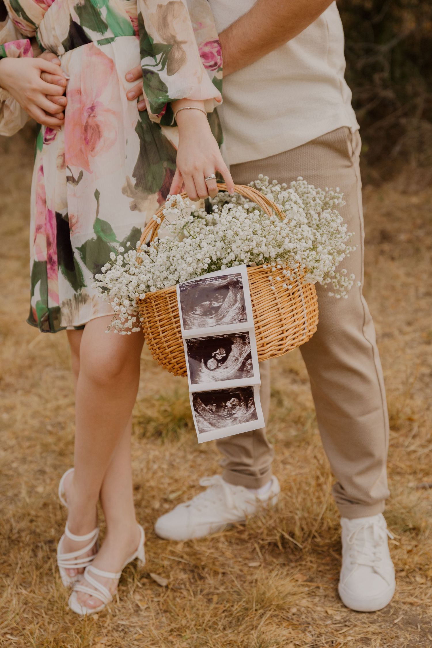Close-up of couple holding wicker basket with ultrasound photos and baby's breath flowers.