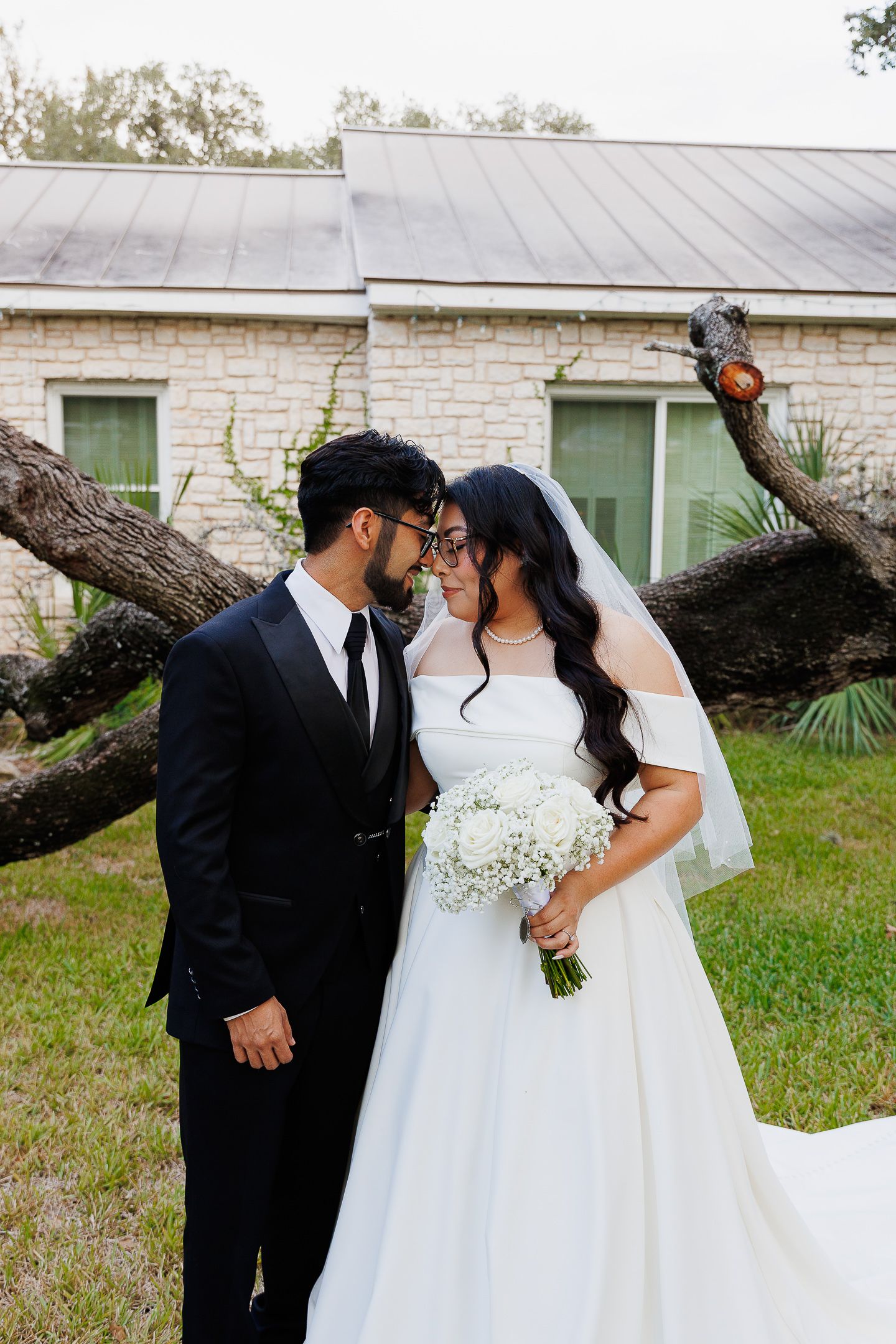 A tender moment between a bride and groom sharing a kiss in front of a white stone building.