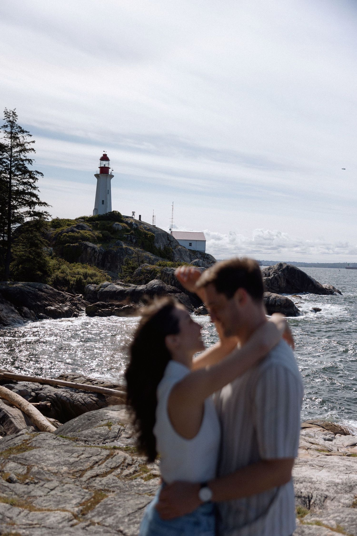 Romantic moment captured near a lighthouse on rocky coastal cliffs.
