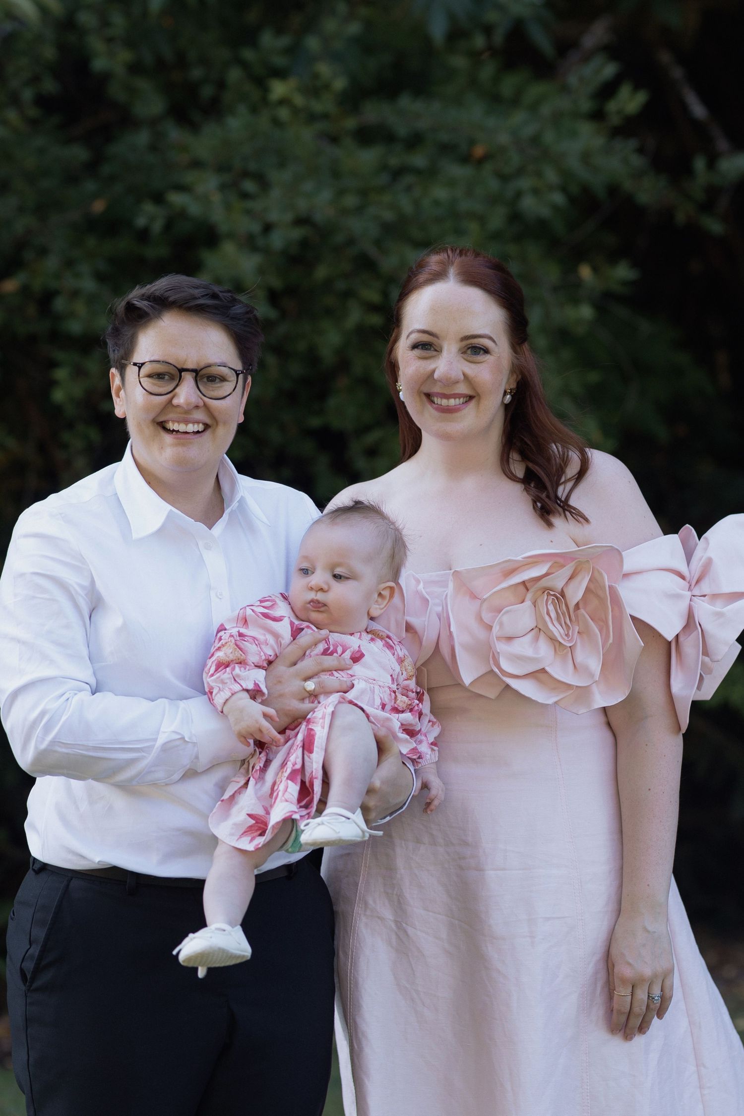 Family members in coordinating pink and white outfits share a tender moment with a baby.