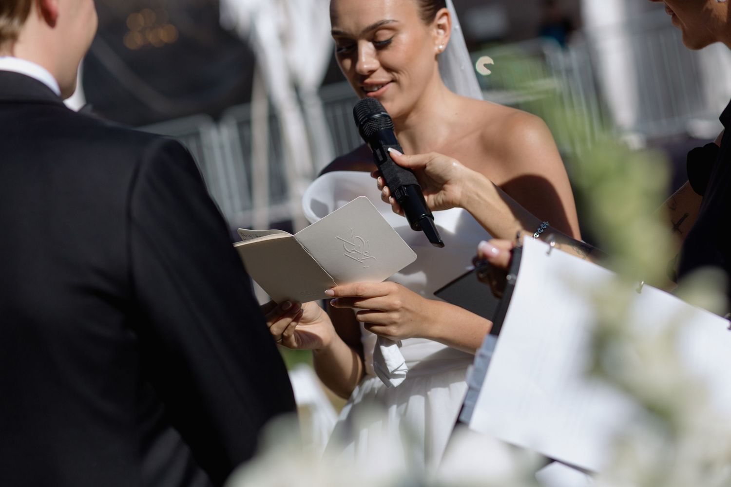 Wedding guests in formal attire hold ceremony programs while seated outdoors.