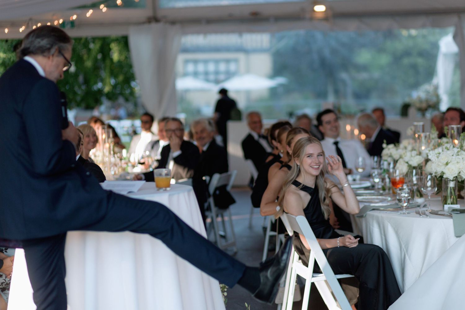Wedding reception venue with elegant table settings and guests under string lights.