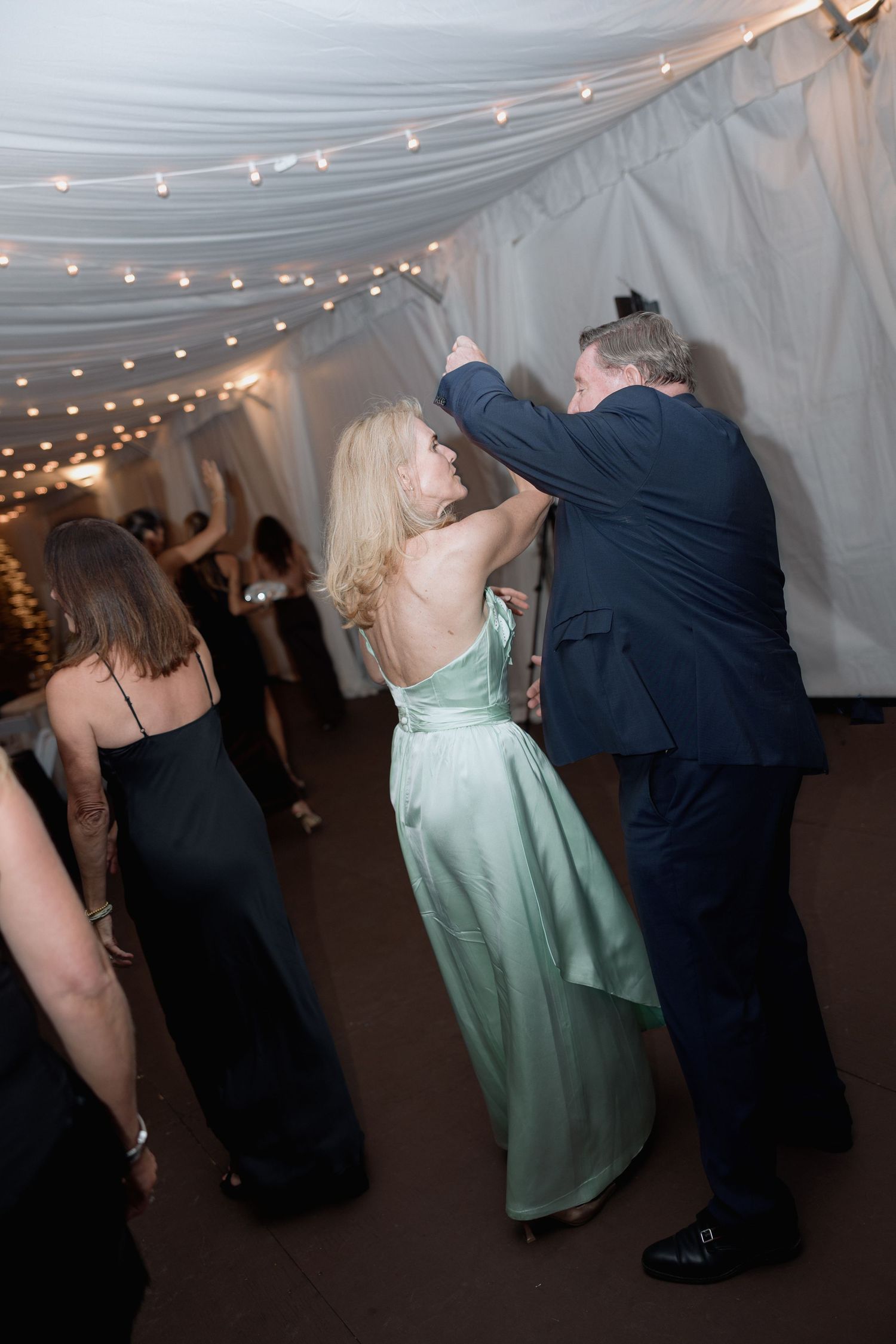 Couples dancing at an elegant reception with string lights and white tent draping.
