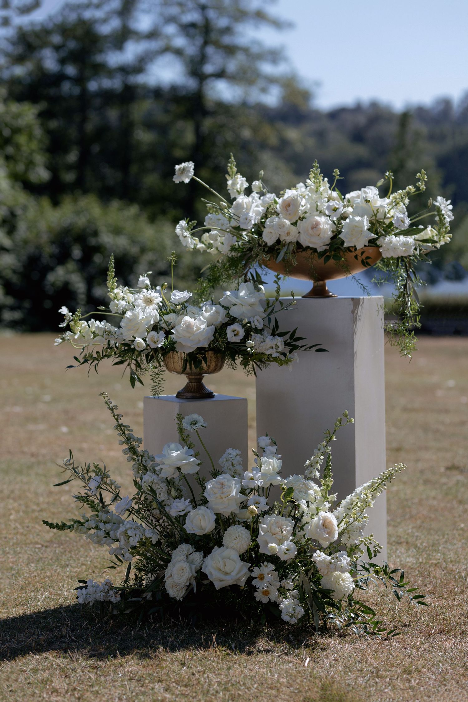Elegant white floral arrangements with roses and greenery placed on pedestals along a ceremony aisle.