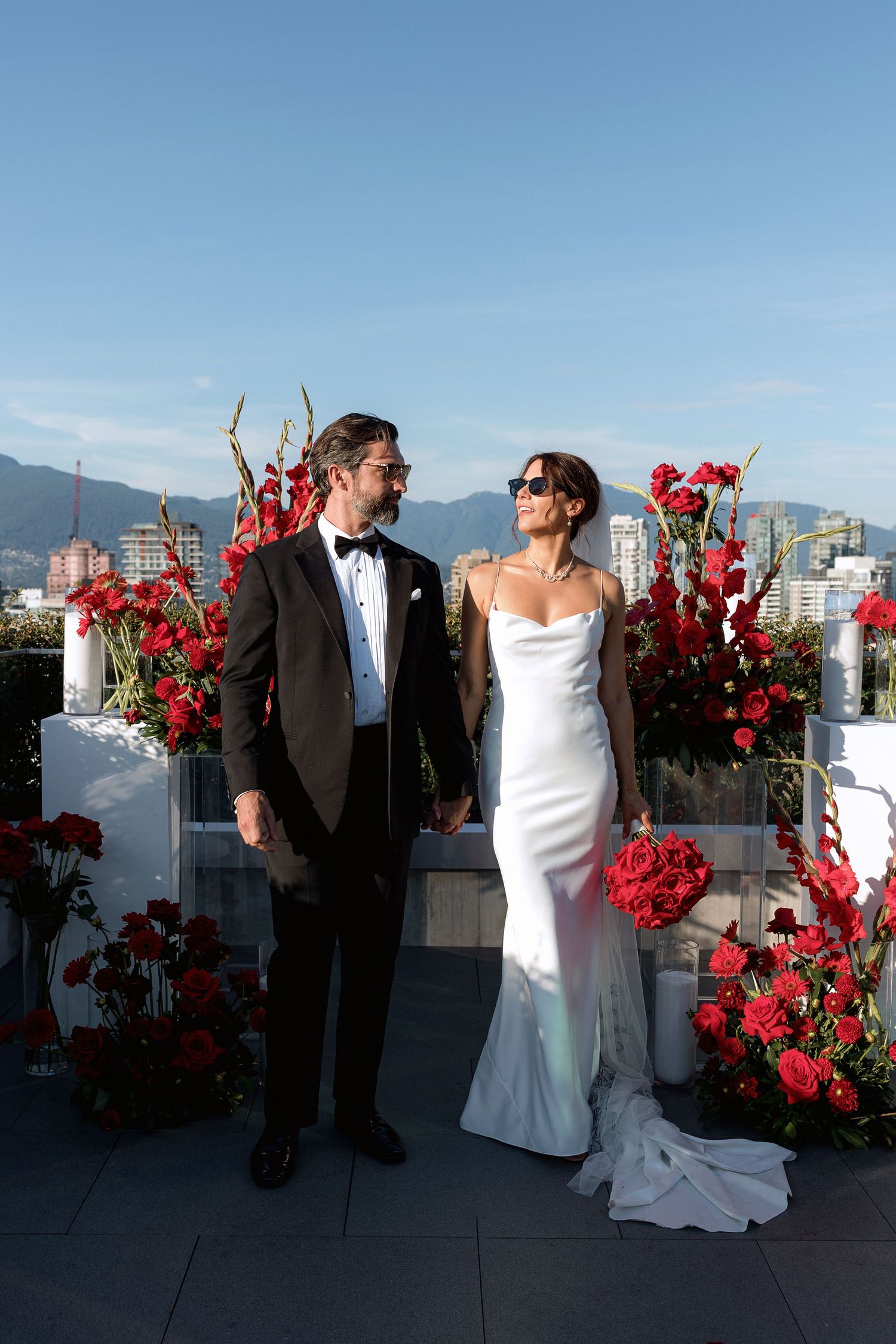 Couple sharing romantic moments during rooftop wedding with red floral decorations.