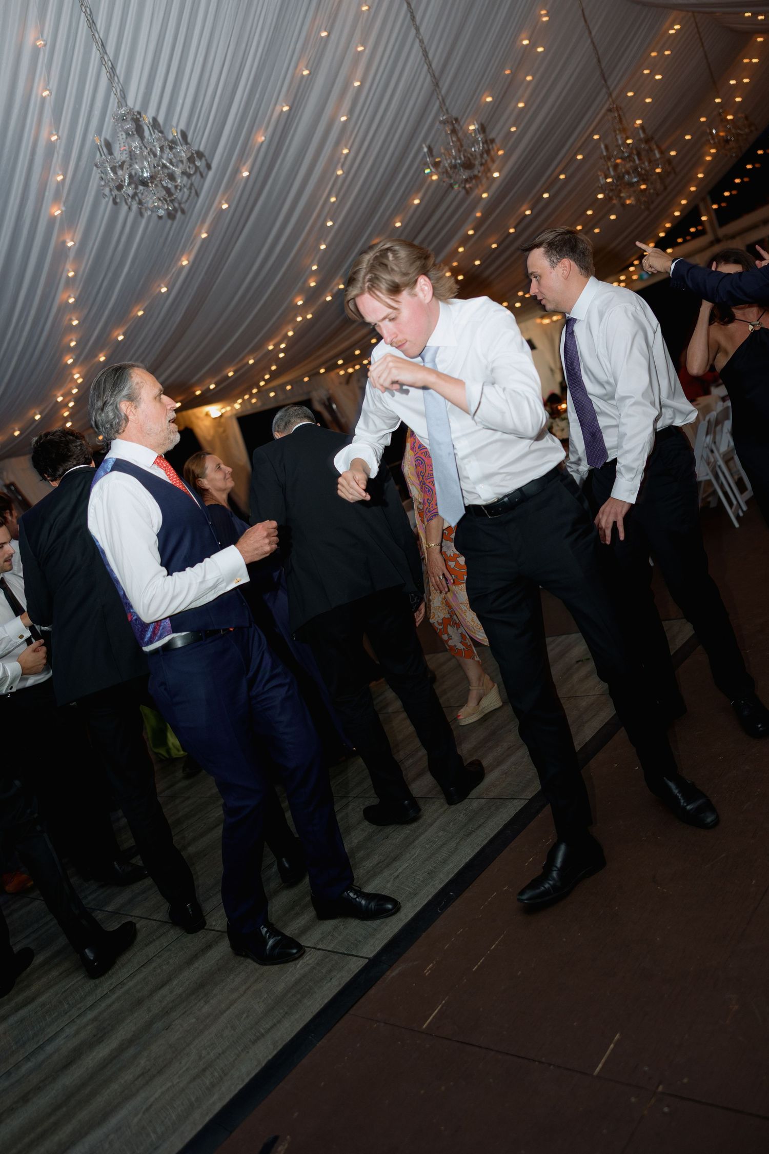 Energetic dance moves on display at a wedding reception under draped lighting.