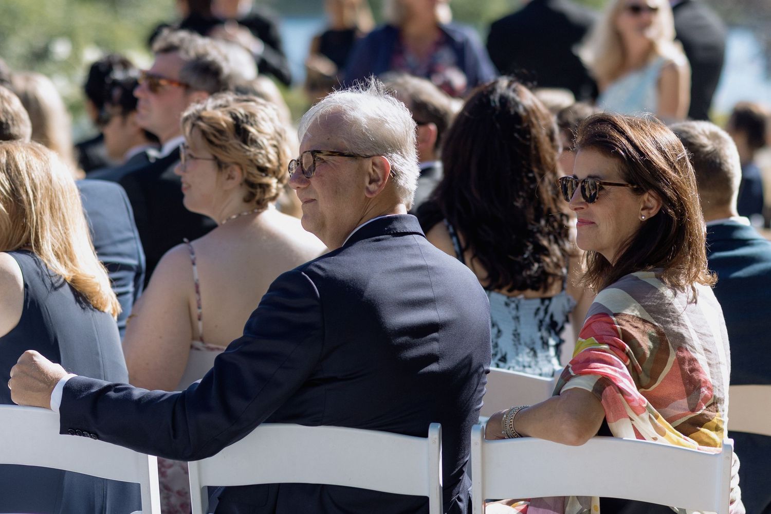Wedding guests seated in white chairs at outdoor ceremony venue.
