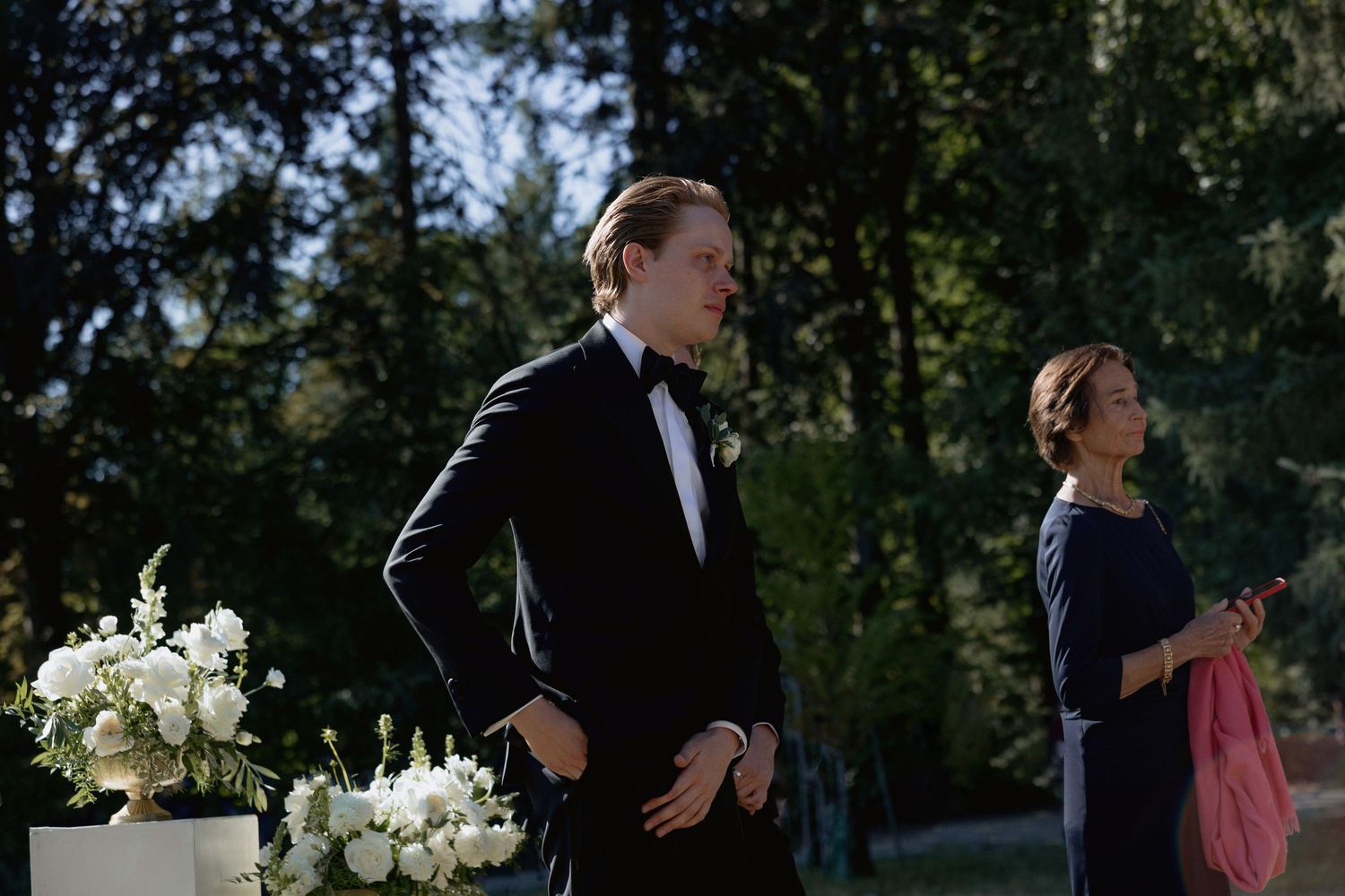 Formal wedding ceremony taking place outdoors with white floral arrangements and guests in attendance.
