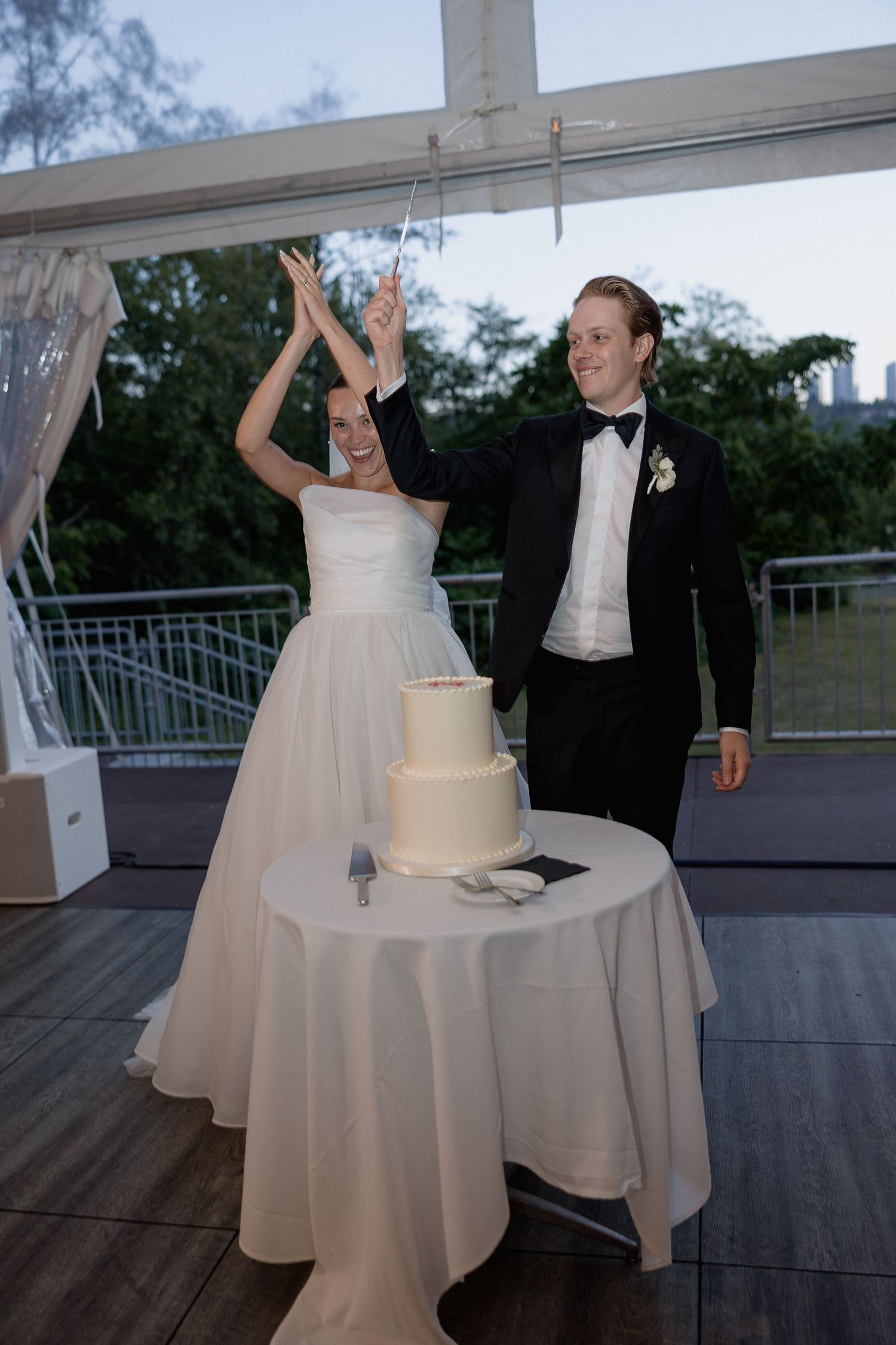 A celebratory moment between newlyweds on an outdoor deck with their wedding cake.