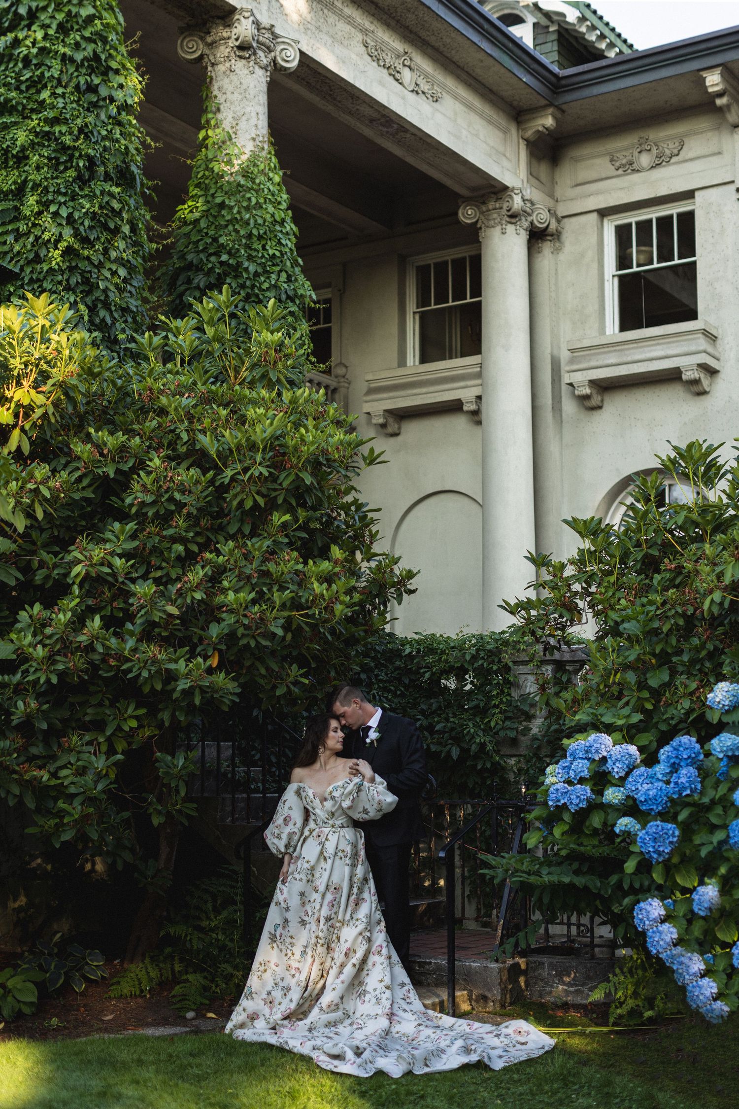 Garden setting with white columns, lush greenery, and blue hydrangeas creating a romantic atmosphere.