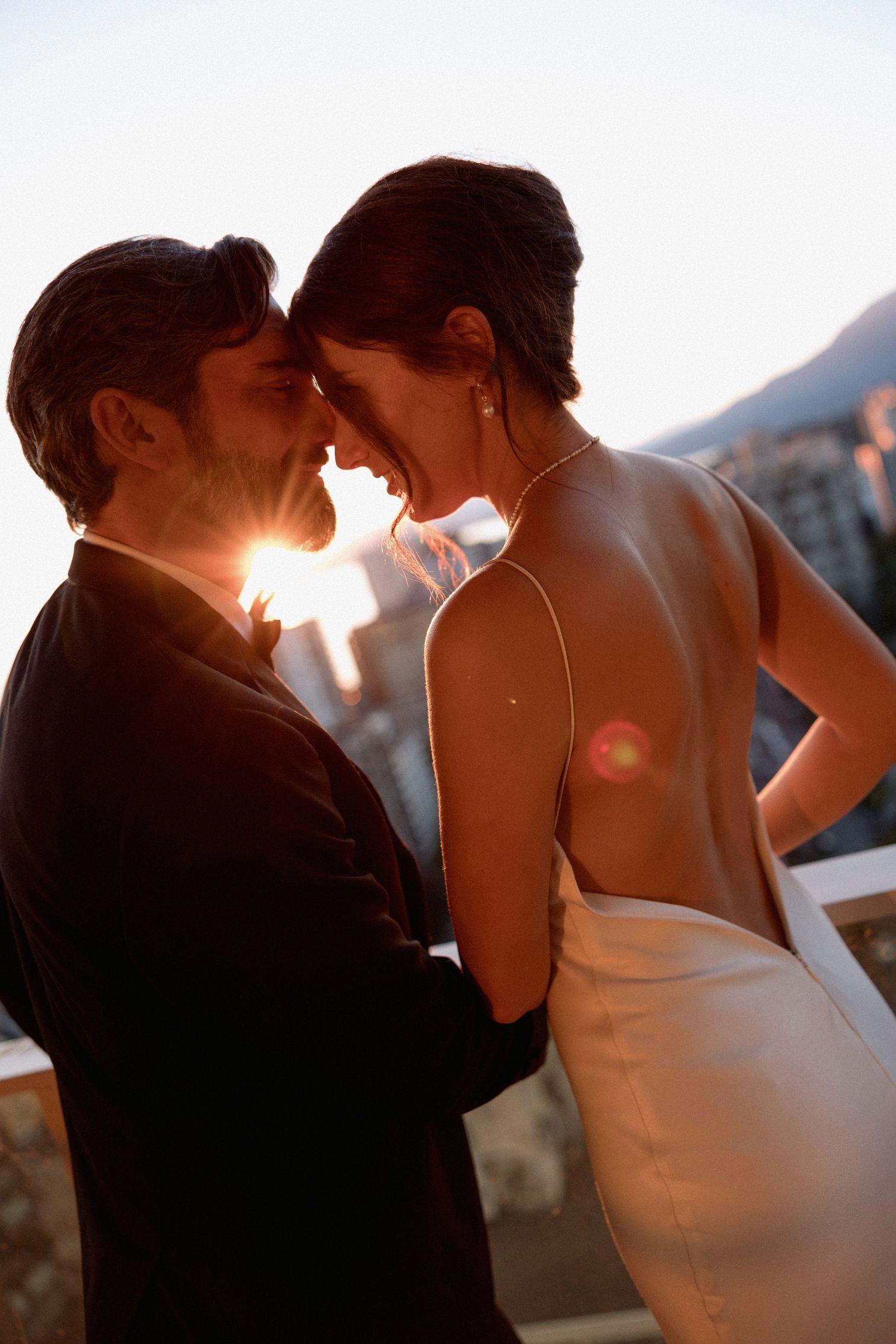 Backlit couple shares romantic moment during sunset with mountain backdrop.