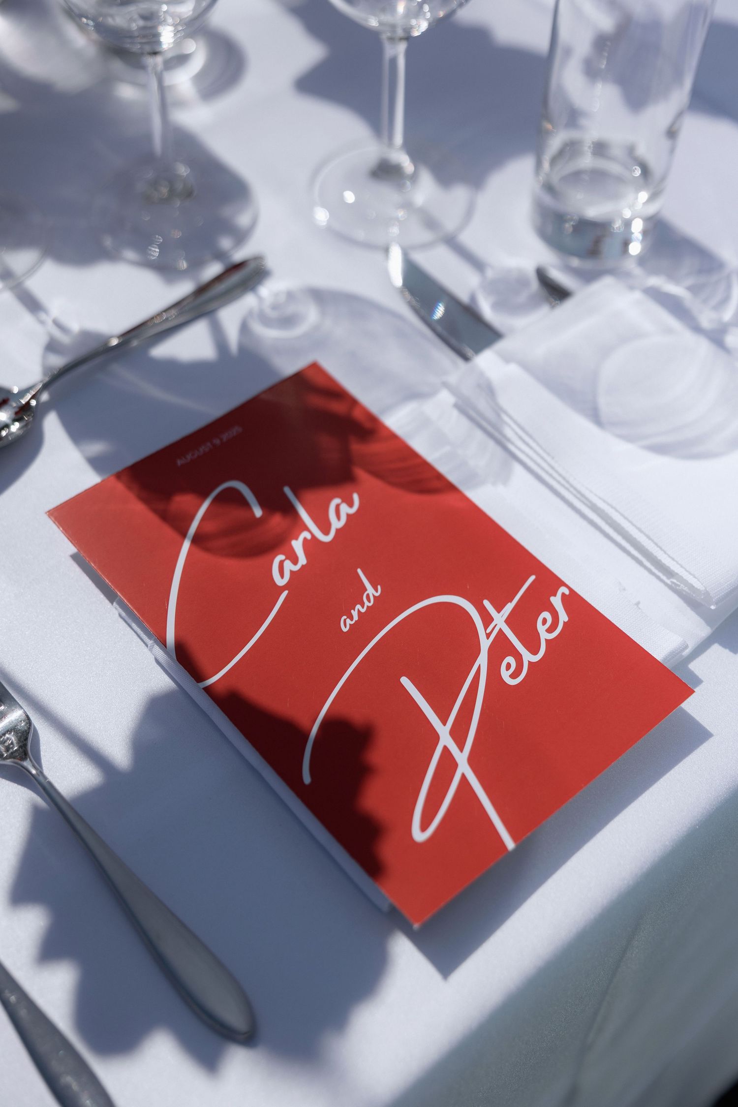 Red place cards with elegant white script handwriting sit among wine glasses on a white tablecloth.