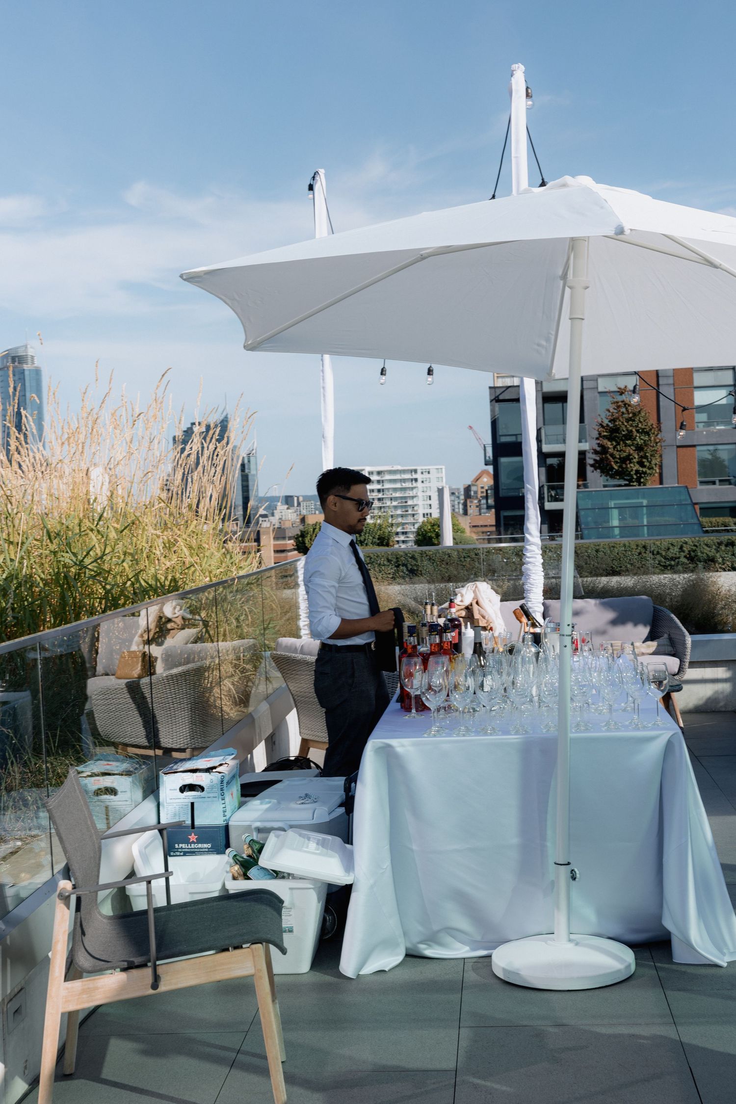 Elegant outdoor rooftop bar setup with white tablecloths and glassware against a city backdrop.