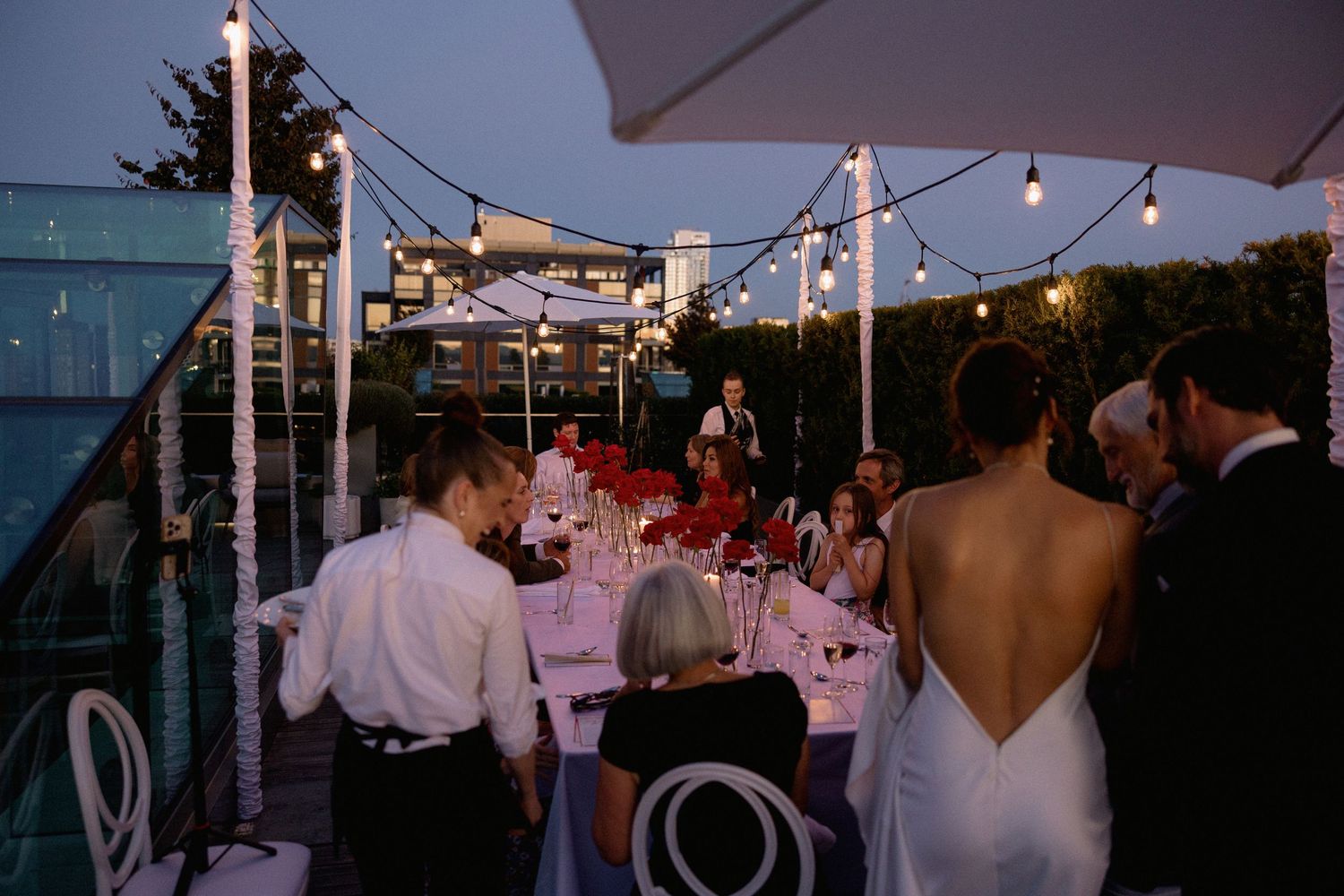 Evening rooftop wedding reception with string lights and white umbrellas.