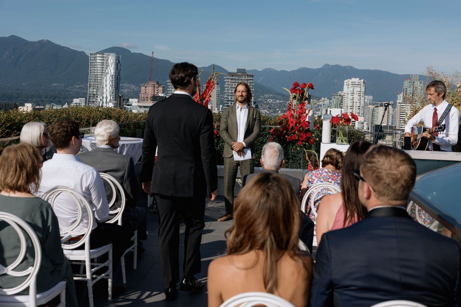 Panoramic view of wedding guests seated outdoors with mountains and city skyline in the background.