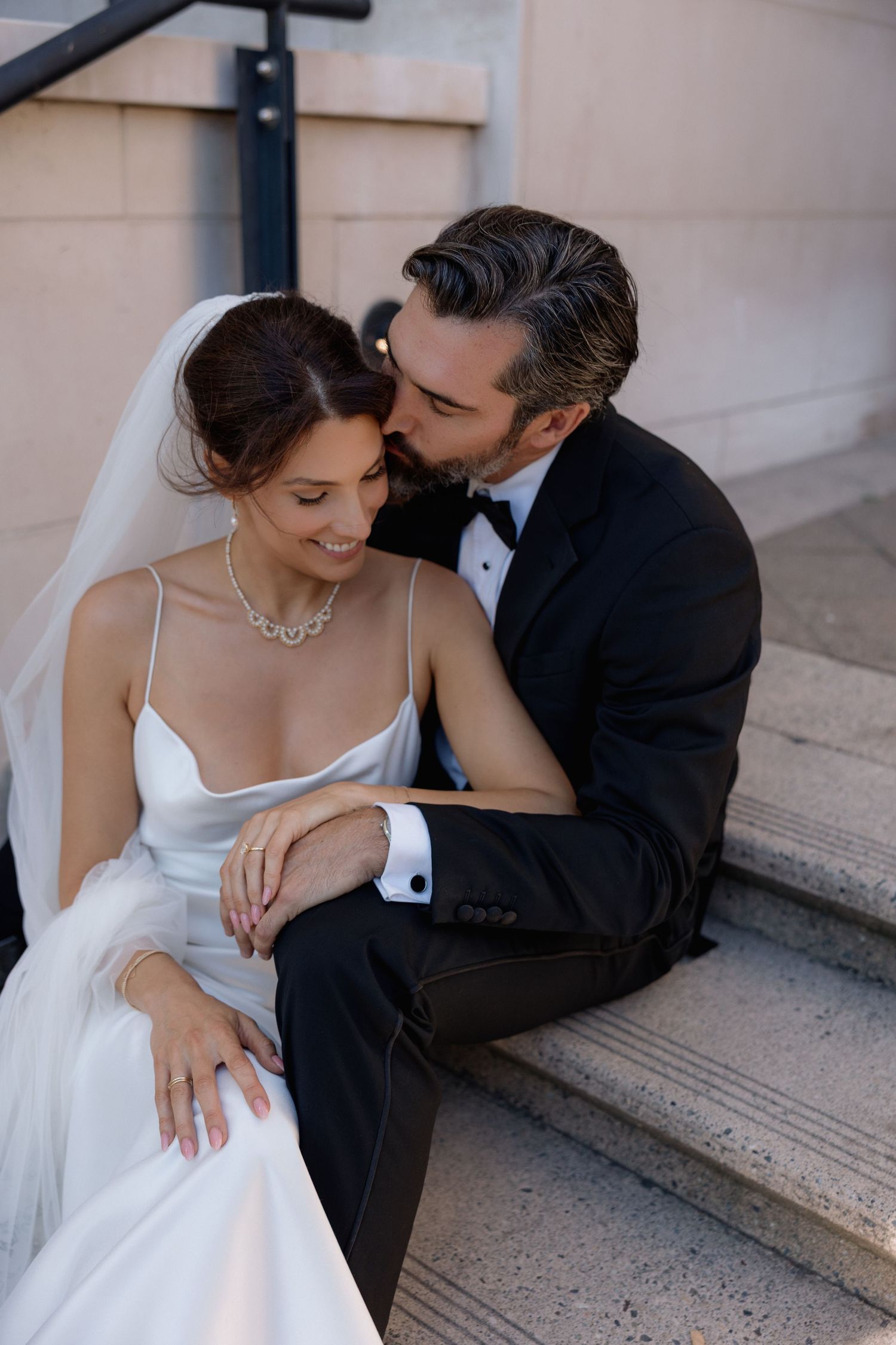 Tender moments between newlyweds sitting on outdoor steps in elegant wedding attire.