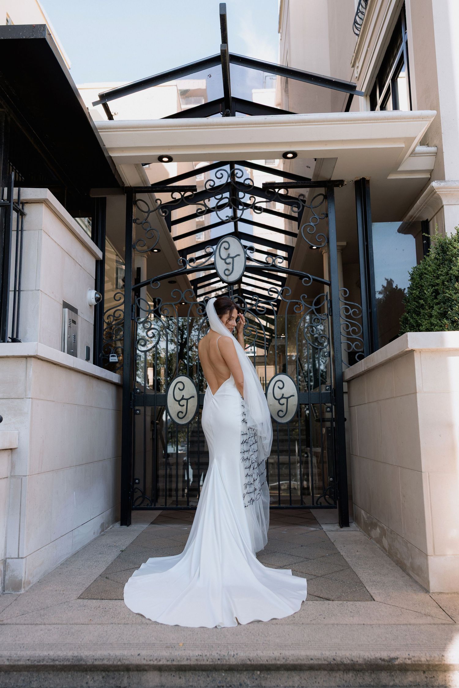 Wedding dress silhouette against modern glass-roofed walkway with architectural details.