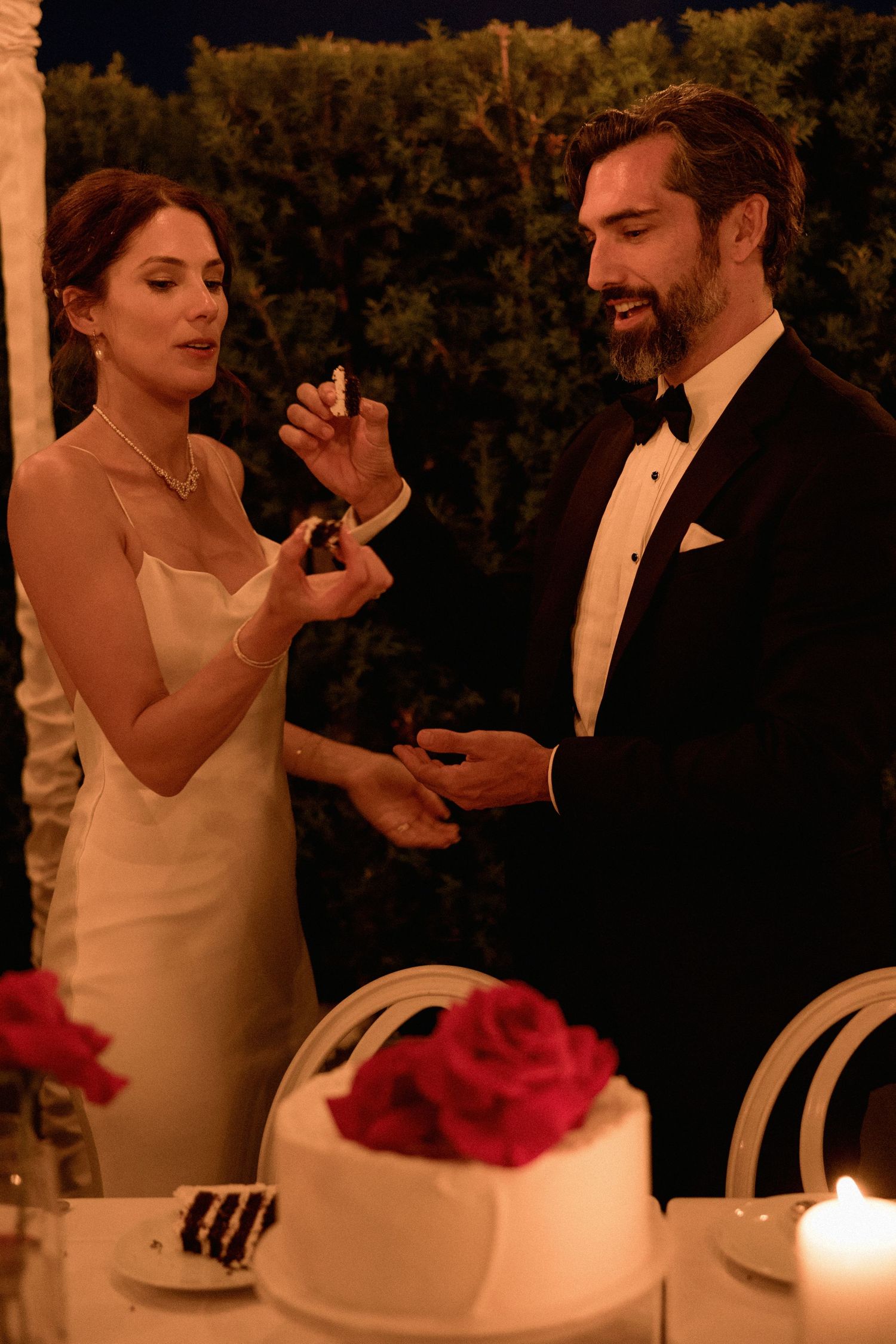 Bride and groom laughing together while cutting their wedding cake at an evening reception in Vancouver