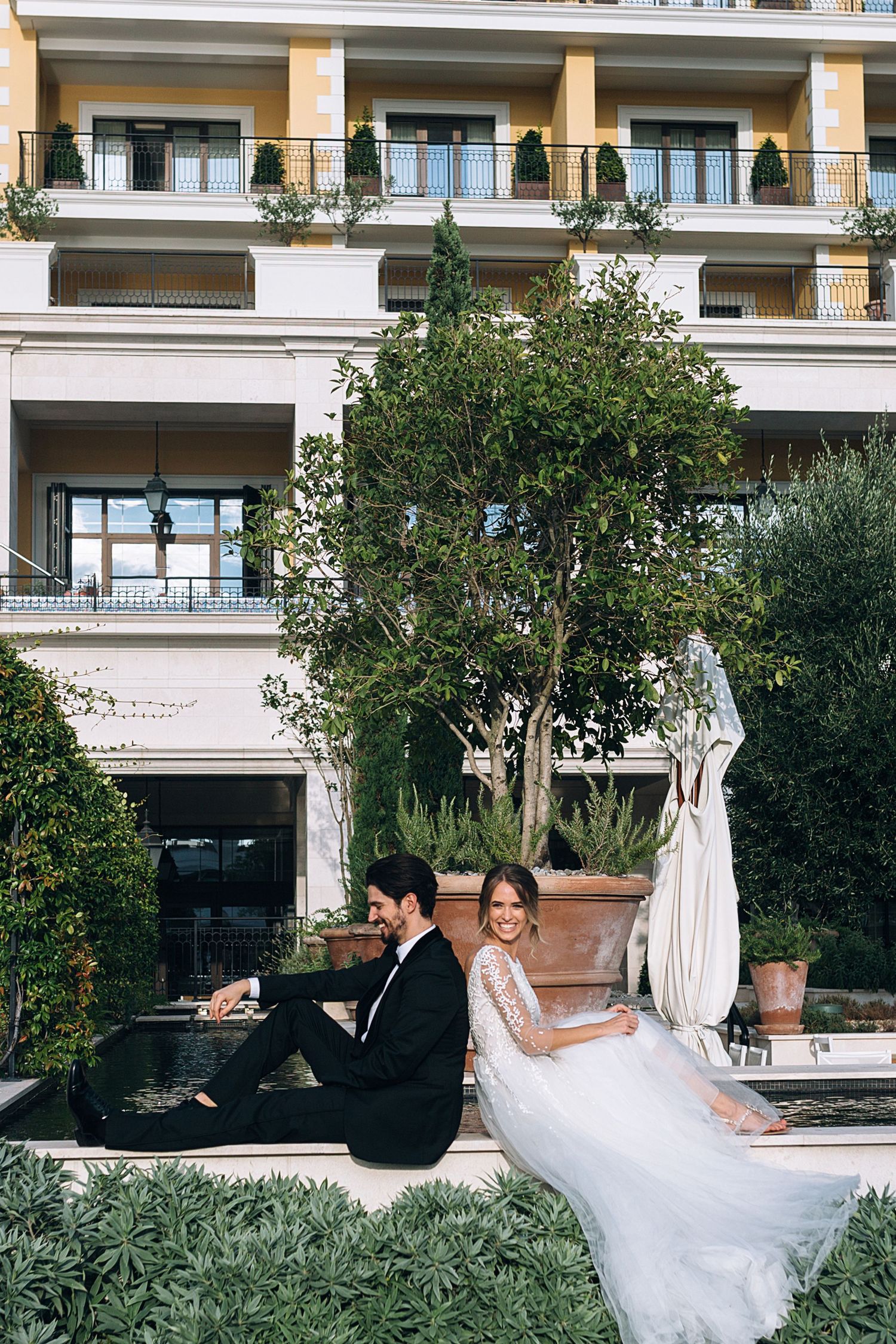 Elegant wedding couple posing in front of a modern building with balconies.