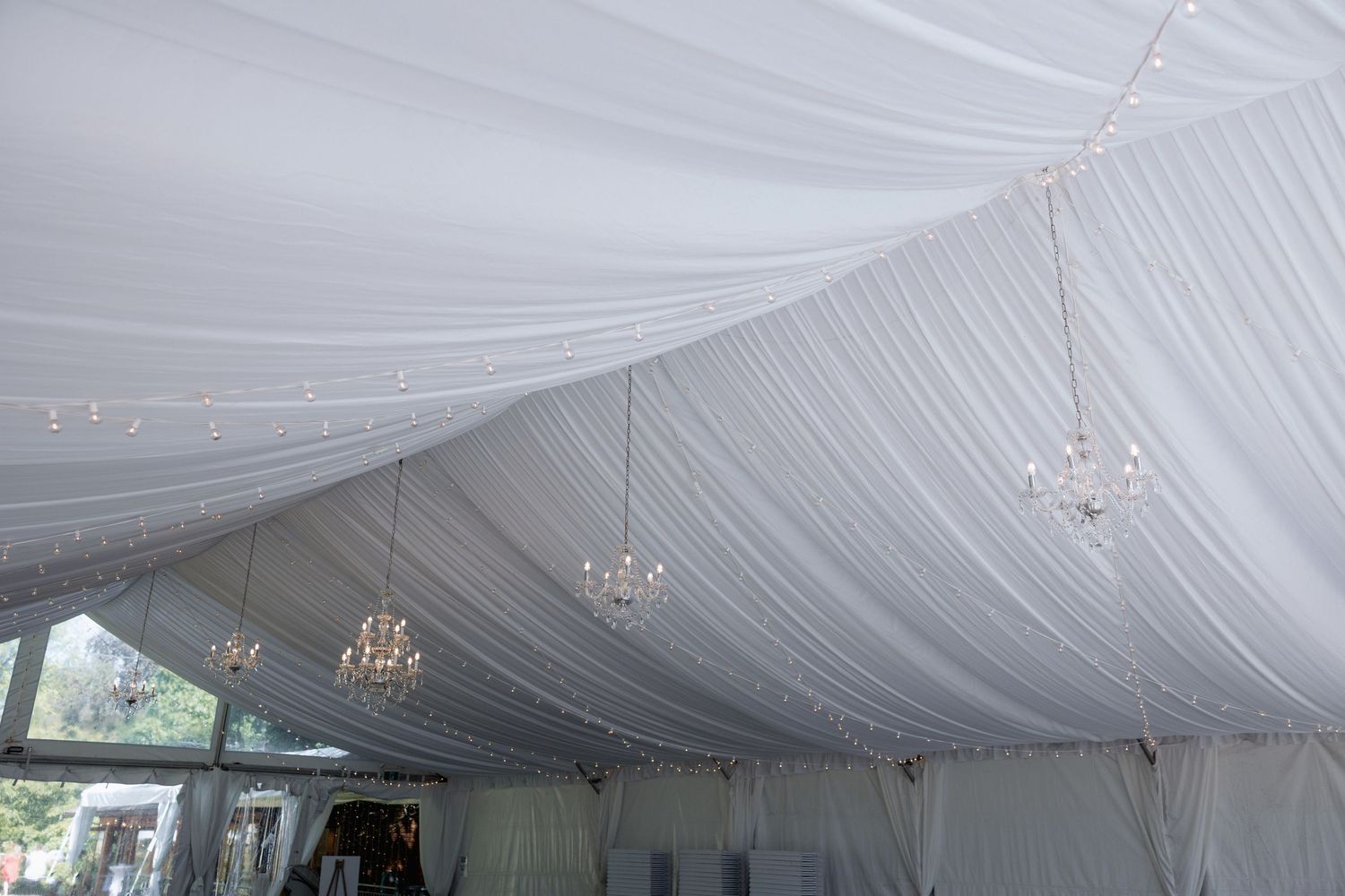 Interior of an elegant white tent with crystal chandeliers and draped fabric ceiling.