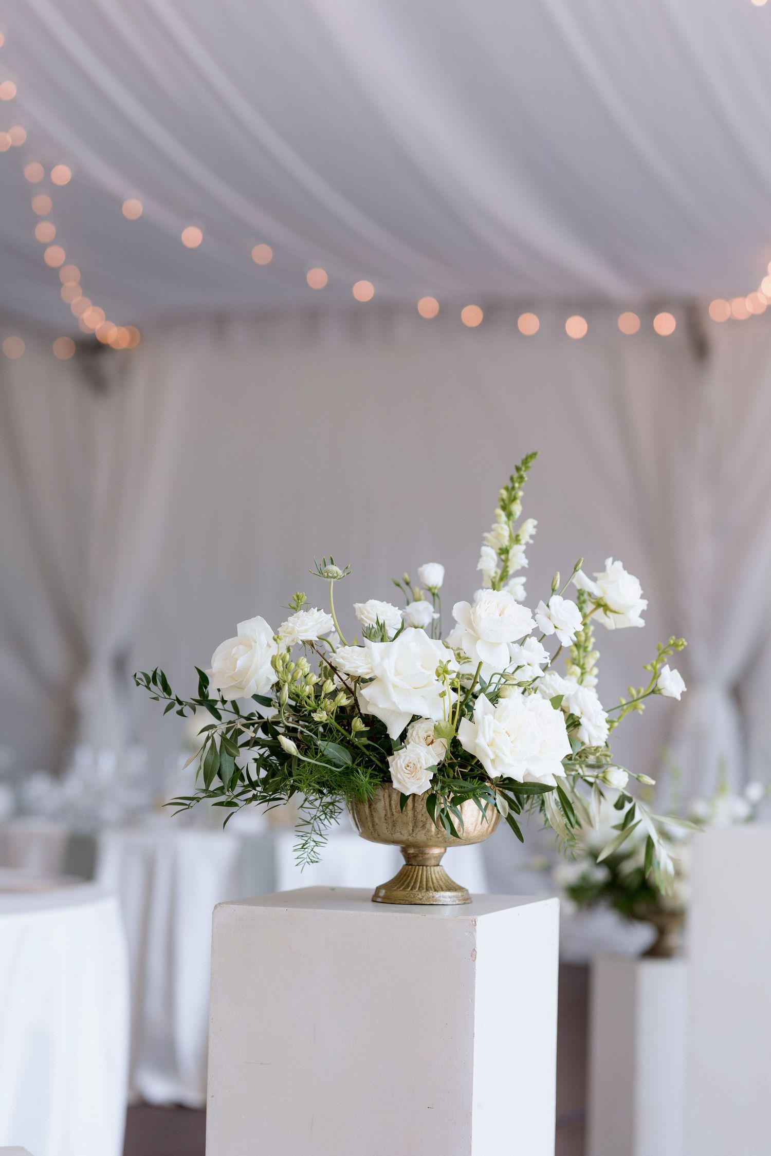 White pedestals with lush white floral arrangements line the reception space.